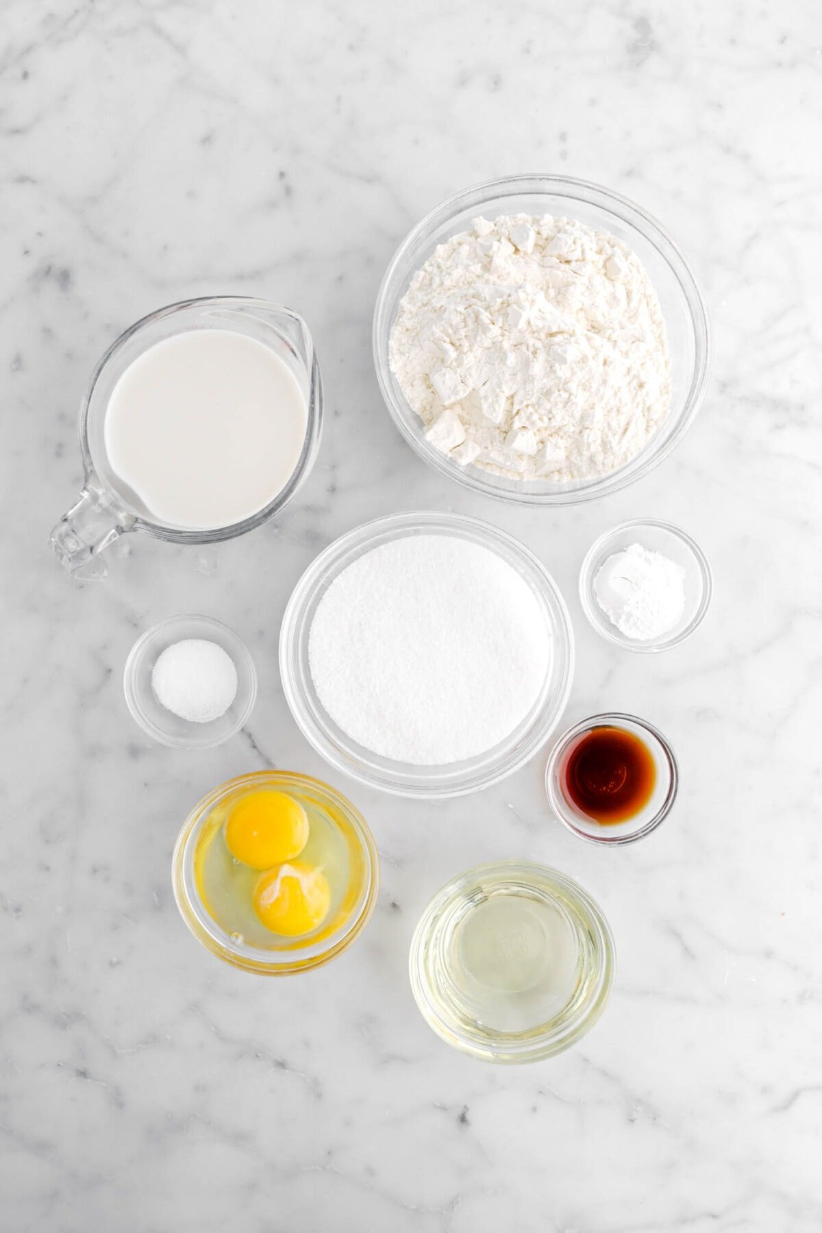 flour, milk, sugar, baking powder, salt, vanilla, oil, and eggs on marble surface.