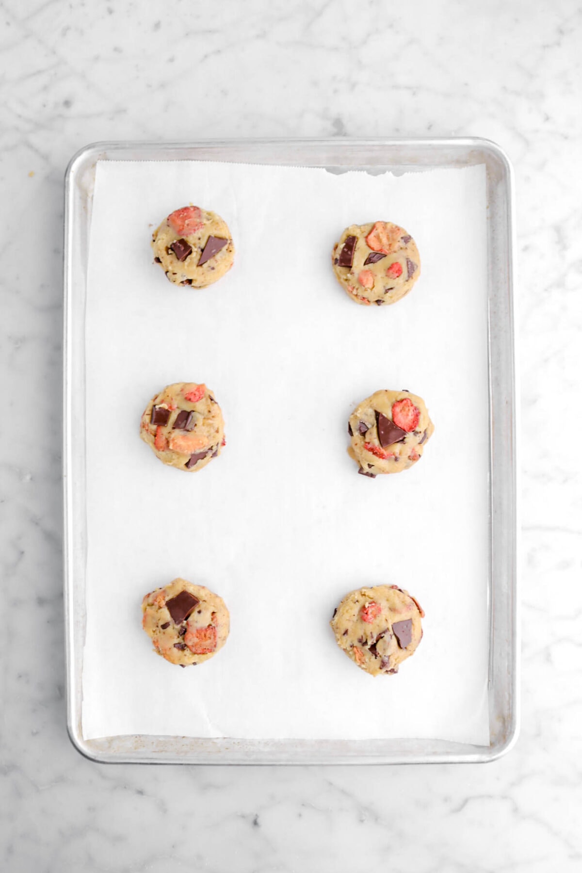 six cookie dough balls on lined sheet pan.