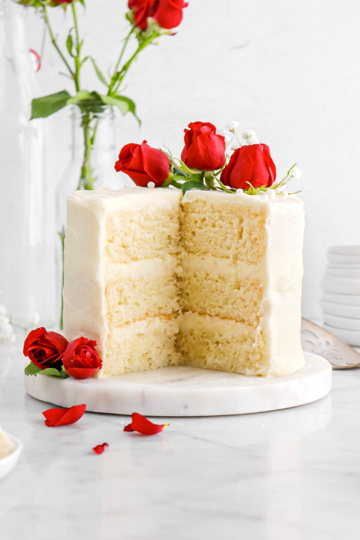close up of cake with two slices missing, red roses on top, and roses beside.