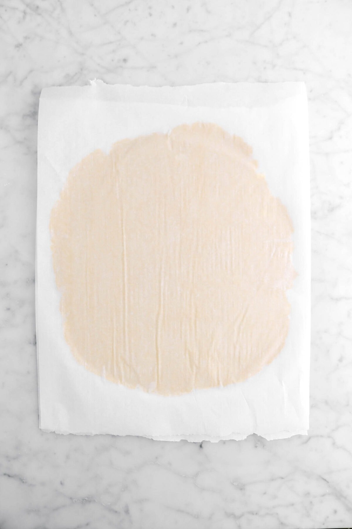 pie dough rolled out in between two sheets of parchment paper.