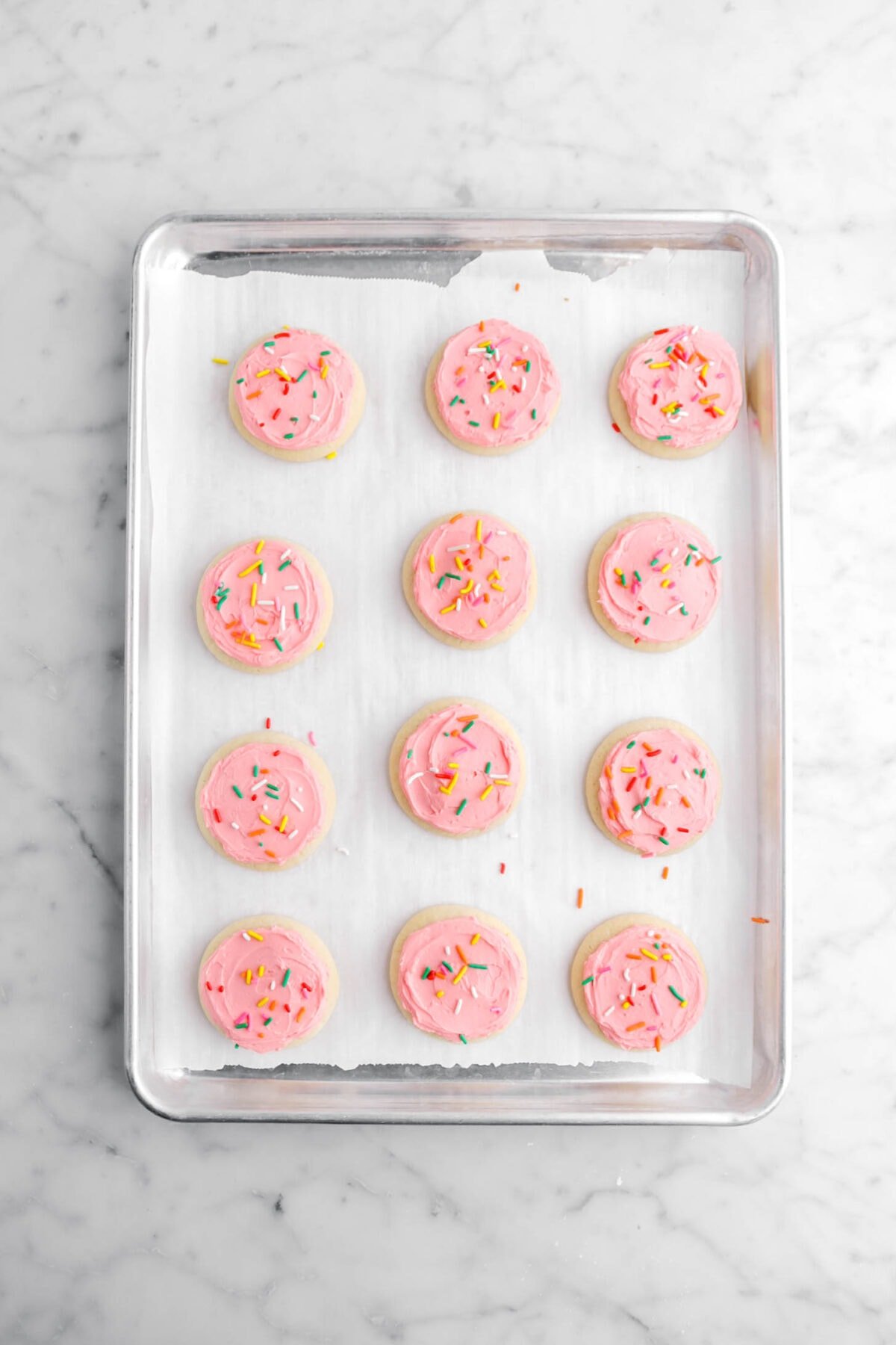 twelve frosted sugar cookies with sprinkles on top on lined sheet pan.