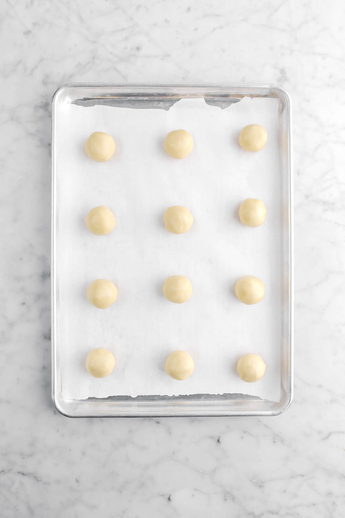 twelve cookie dough balls on lined sheet pan.