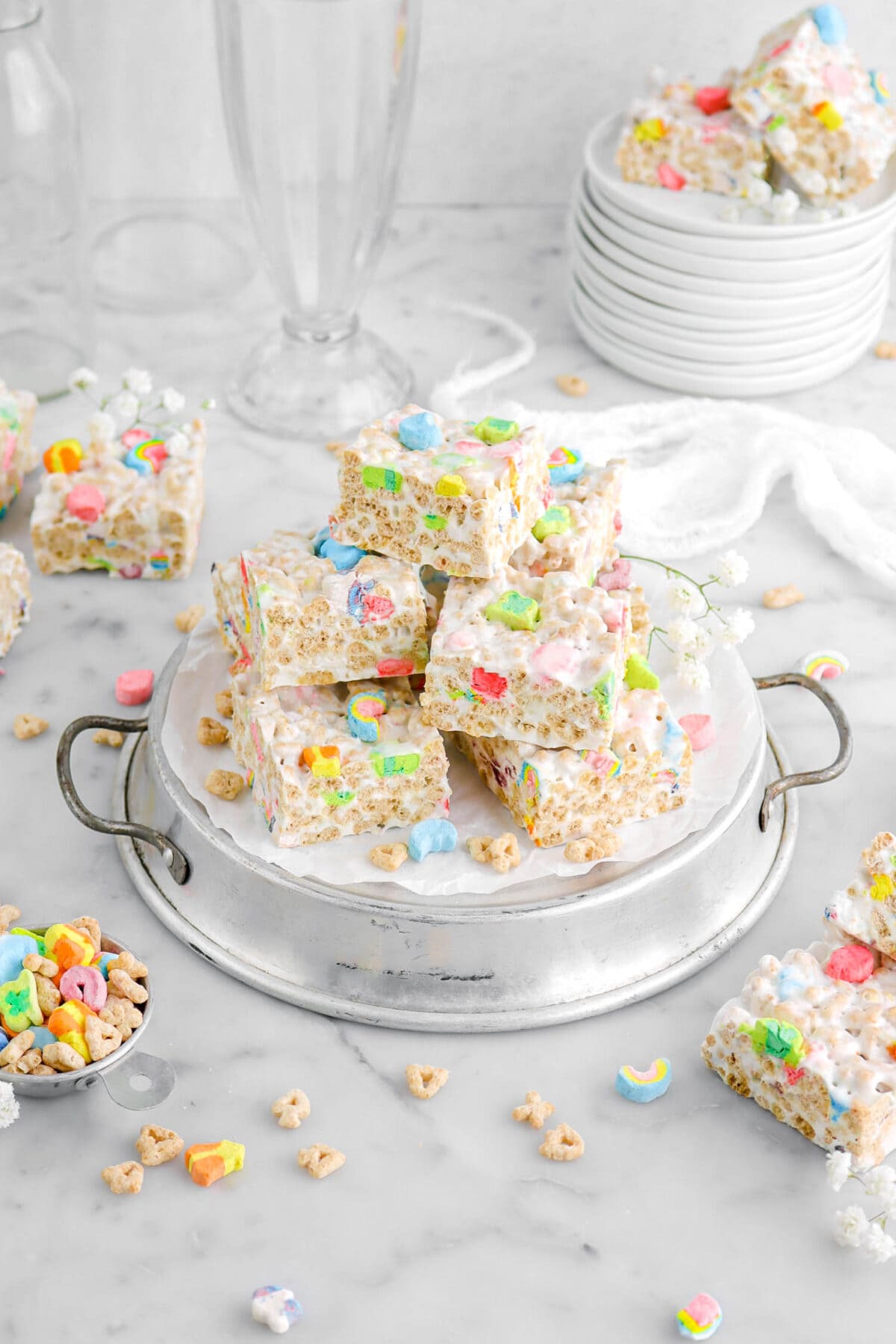 angled shot of stacked lucky charms marshmallow treats with more cereal and marshmallow treats around on marble surface.