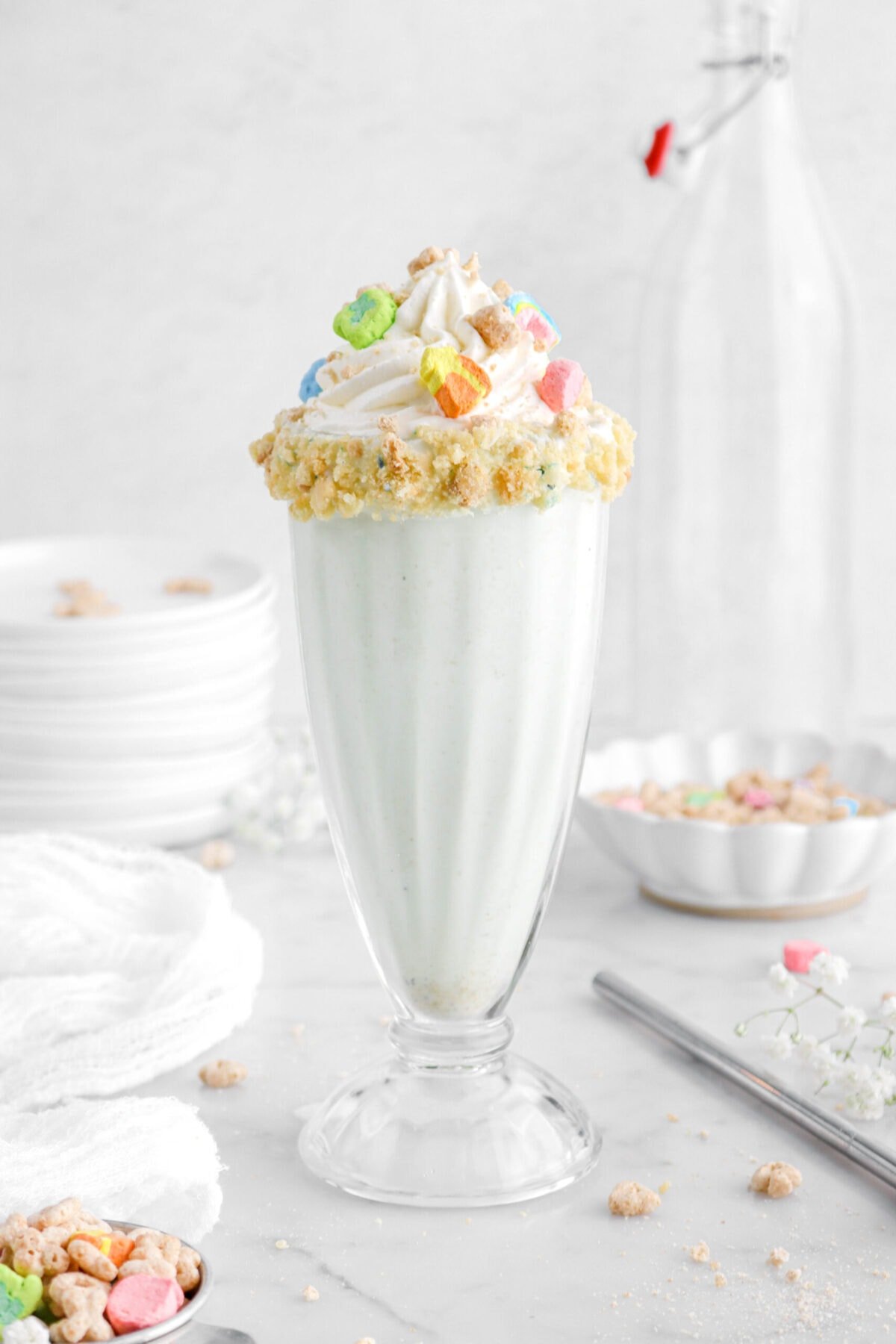 close up front shot of lucky charms milkshake in tall milkshake glass with whipped cream and cereal on top.