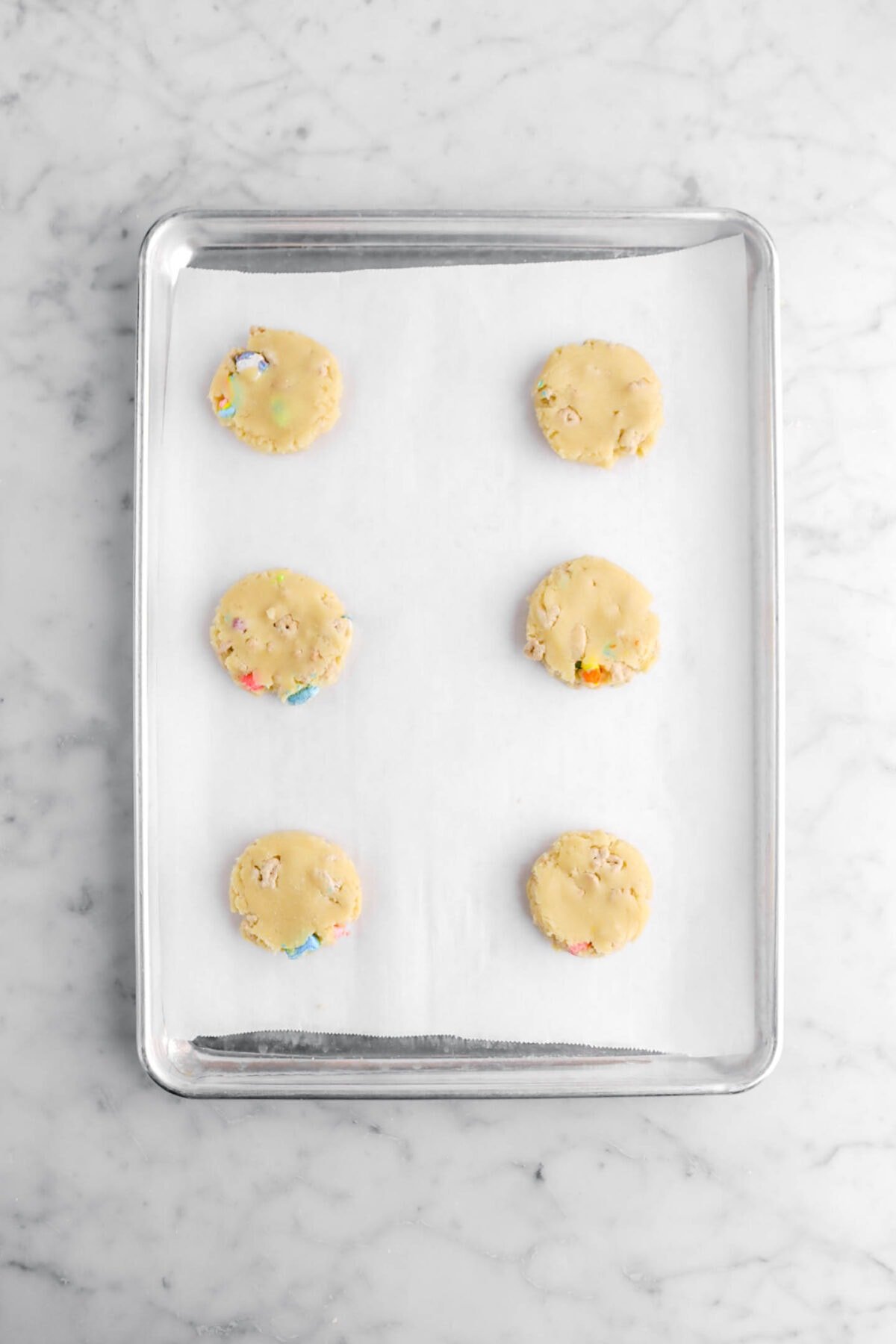 six cookie dough balls flatted on lined sheet pan.