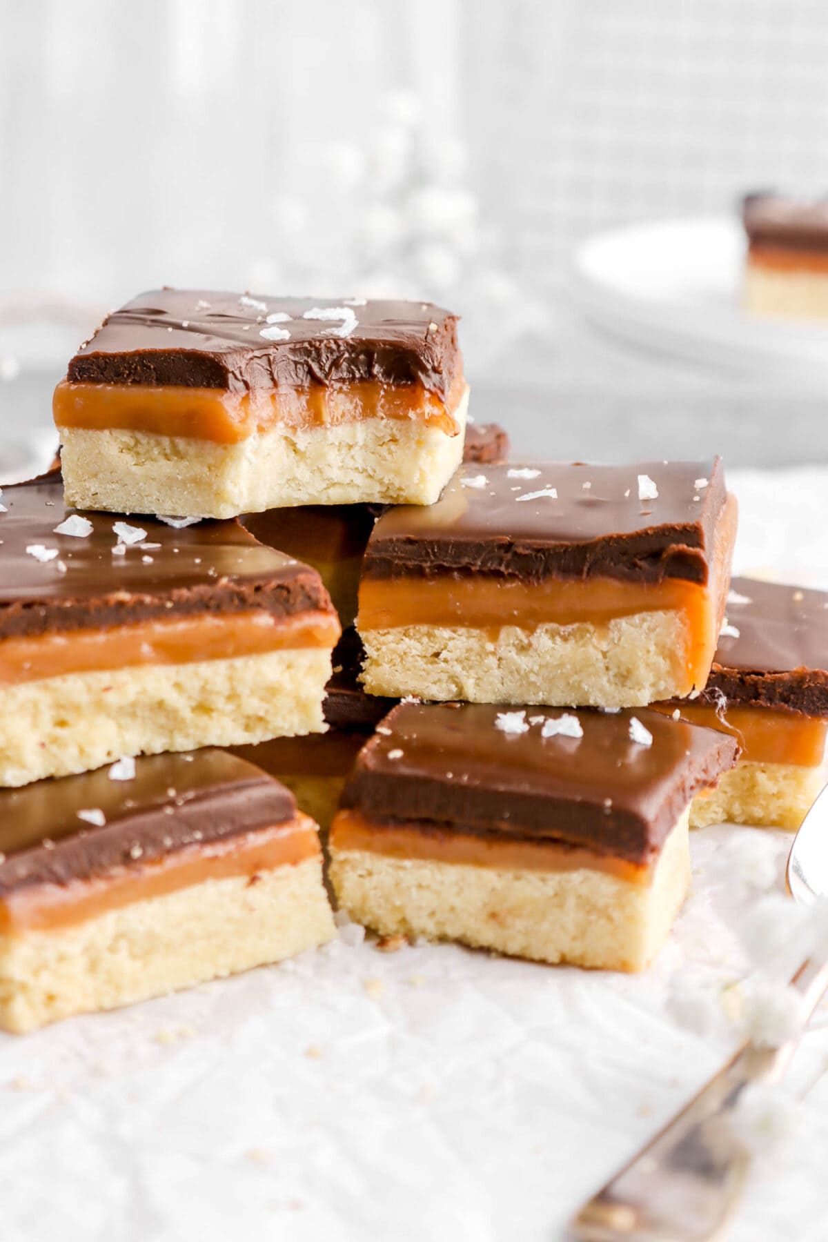 close up of piled millionaire's shortbread bars on parchment paper with spoon beside.