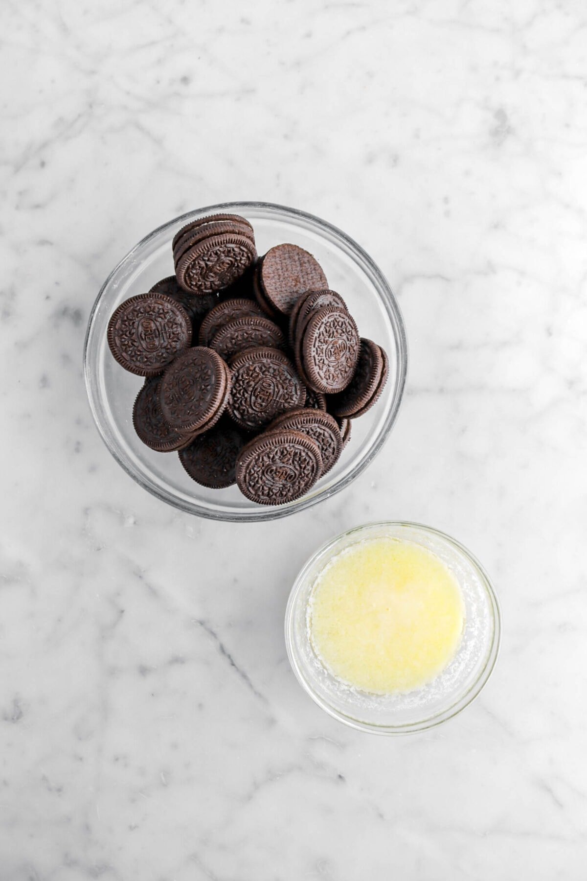 oreos and melted butter in two glass bowls on marble surface.