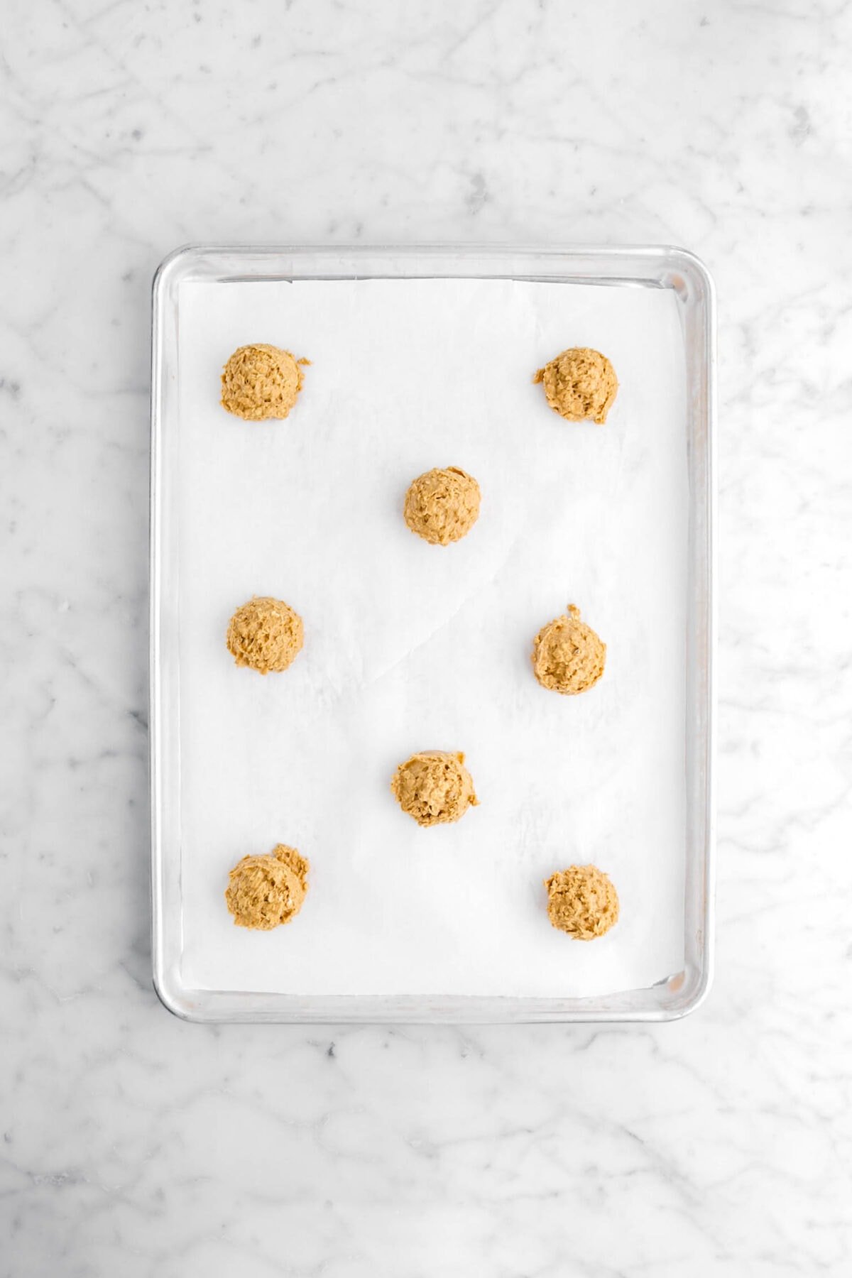 eight cookie dough balls on lined sheet pan.