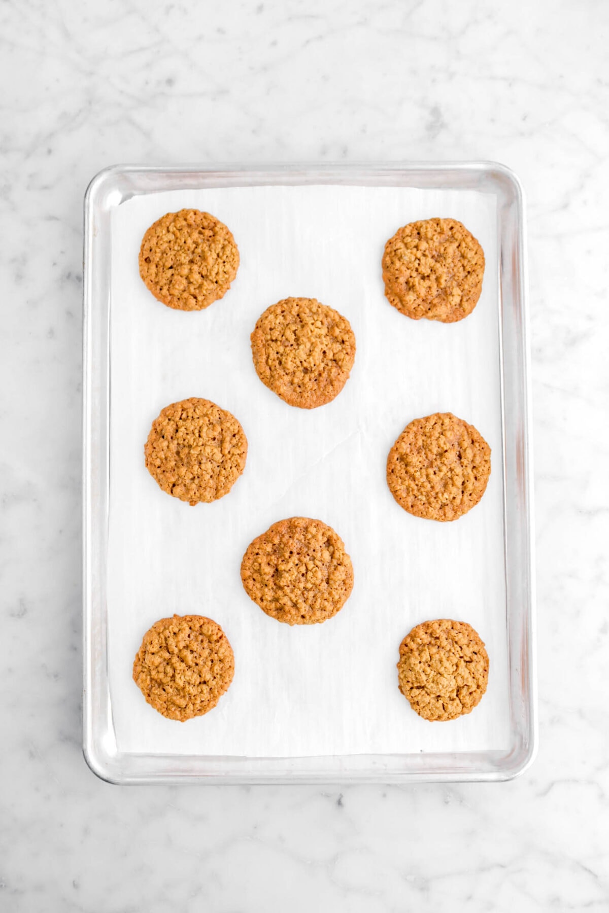 eight baked oatmeal cookies on lined sheet pan.