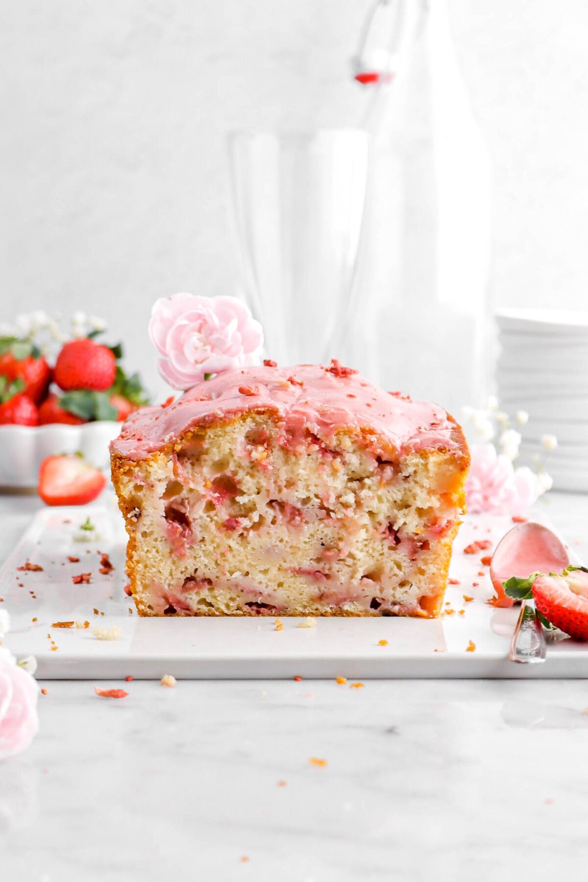 close up of cut strawberry bread on white tray with a pink carnation on top and fresh strawberries around.