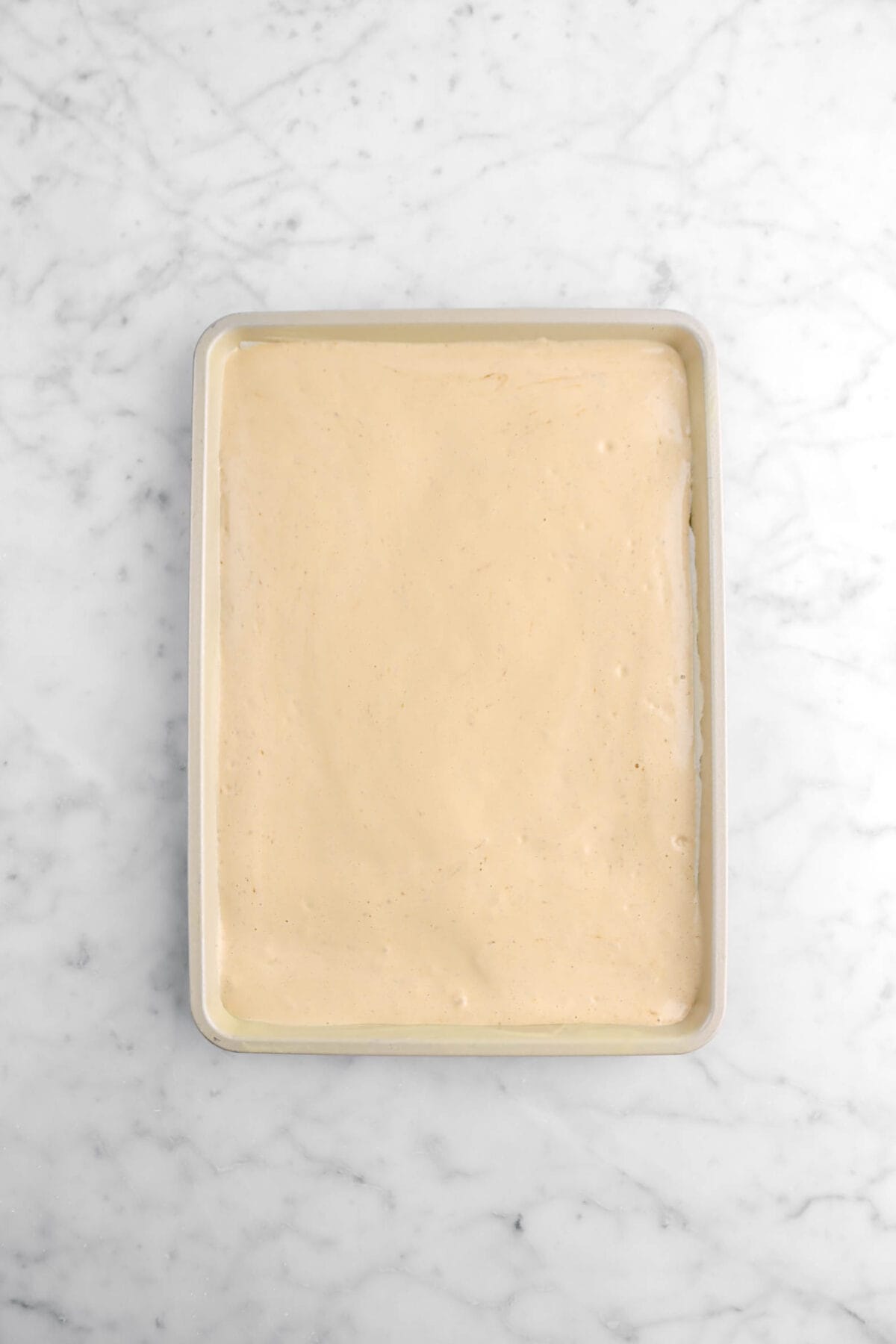 genoise batter in gold sheet pan on marble surface.
