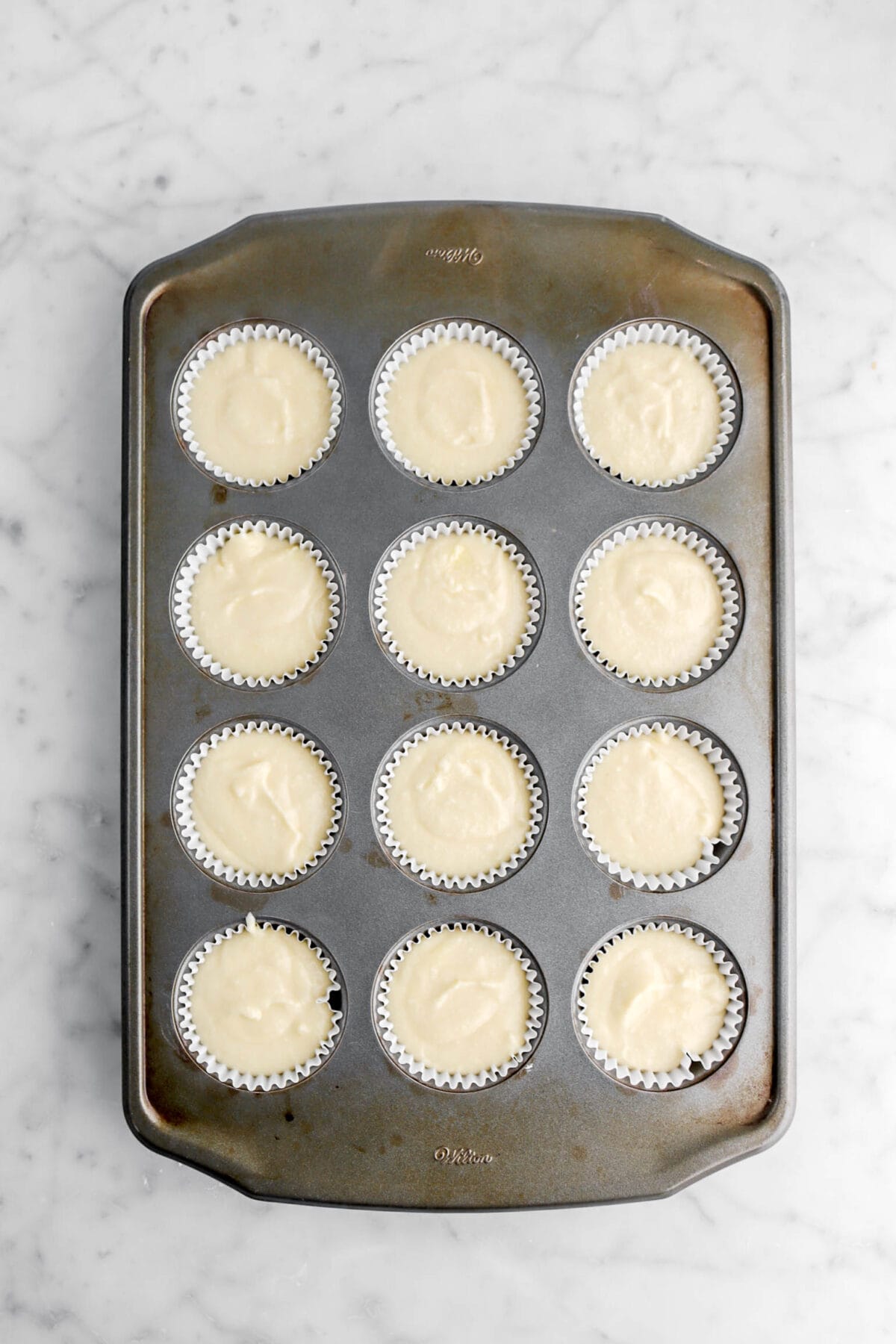 cake batter in twelve lined cavities in cupcake pan.