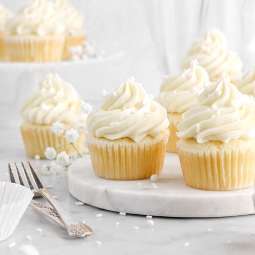 vanilla cupcakes on marble surface with white flowers and forks beside.