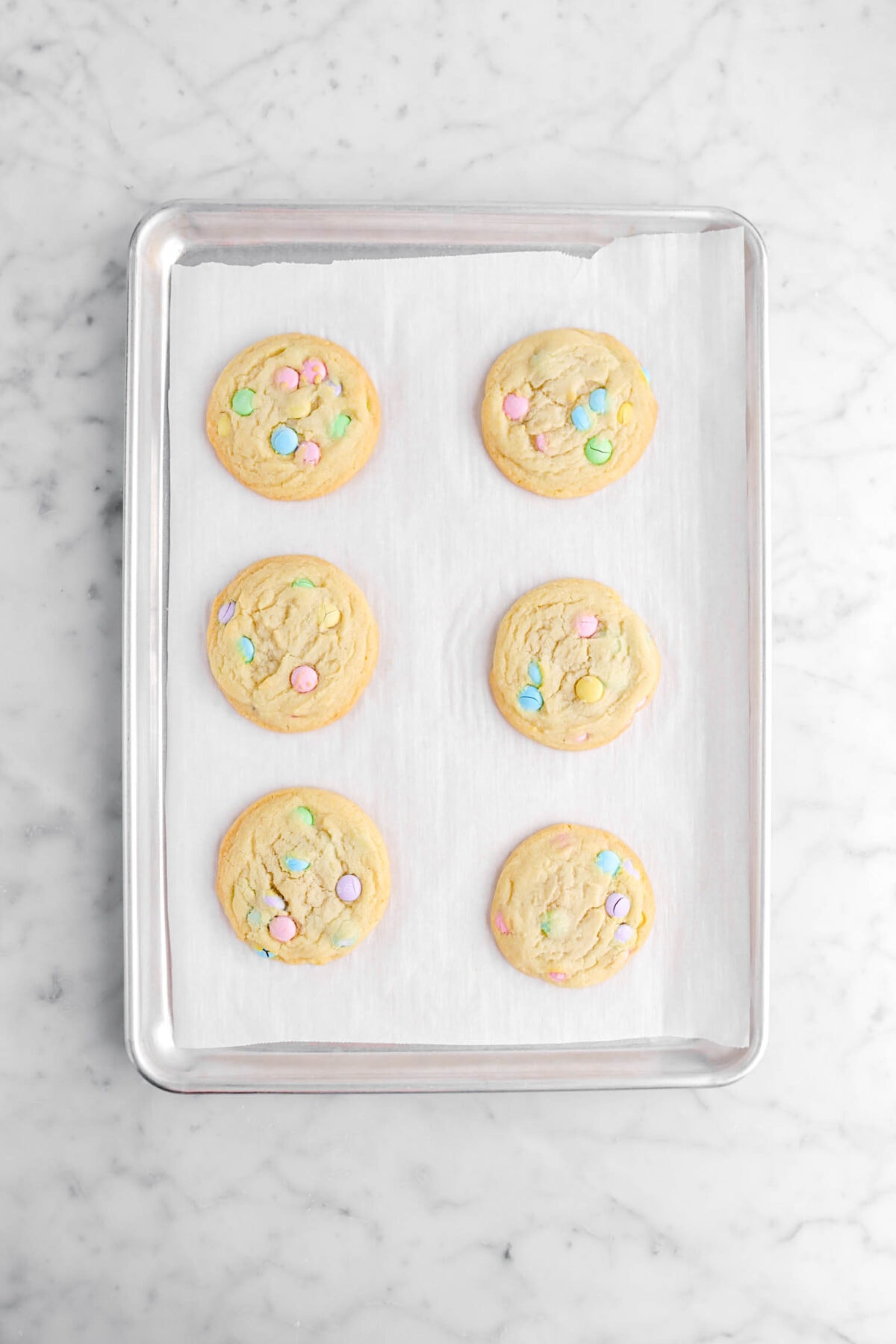 six baked M&M sugar cookies on lined sheet pan.