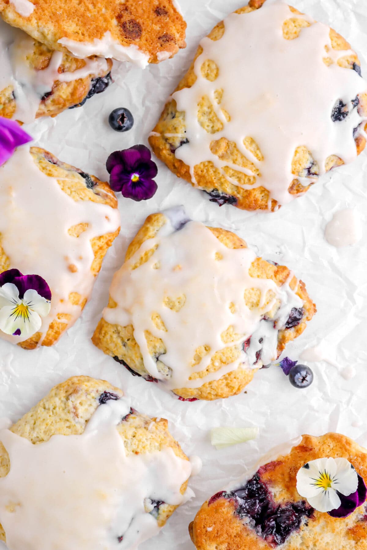 close up overhead shot of blueberry white chocolate scone with more scones around and purple and white flowers.