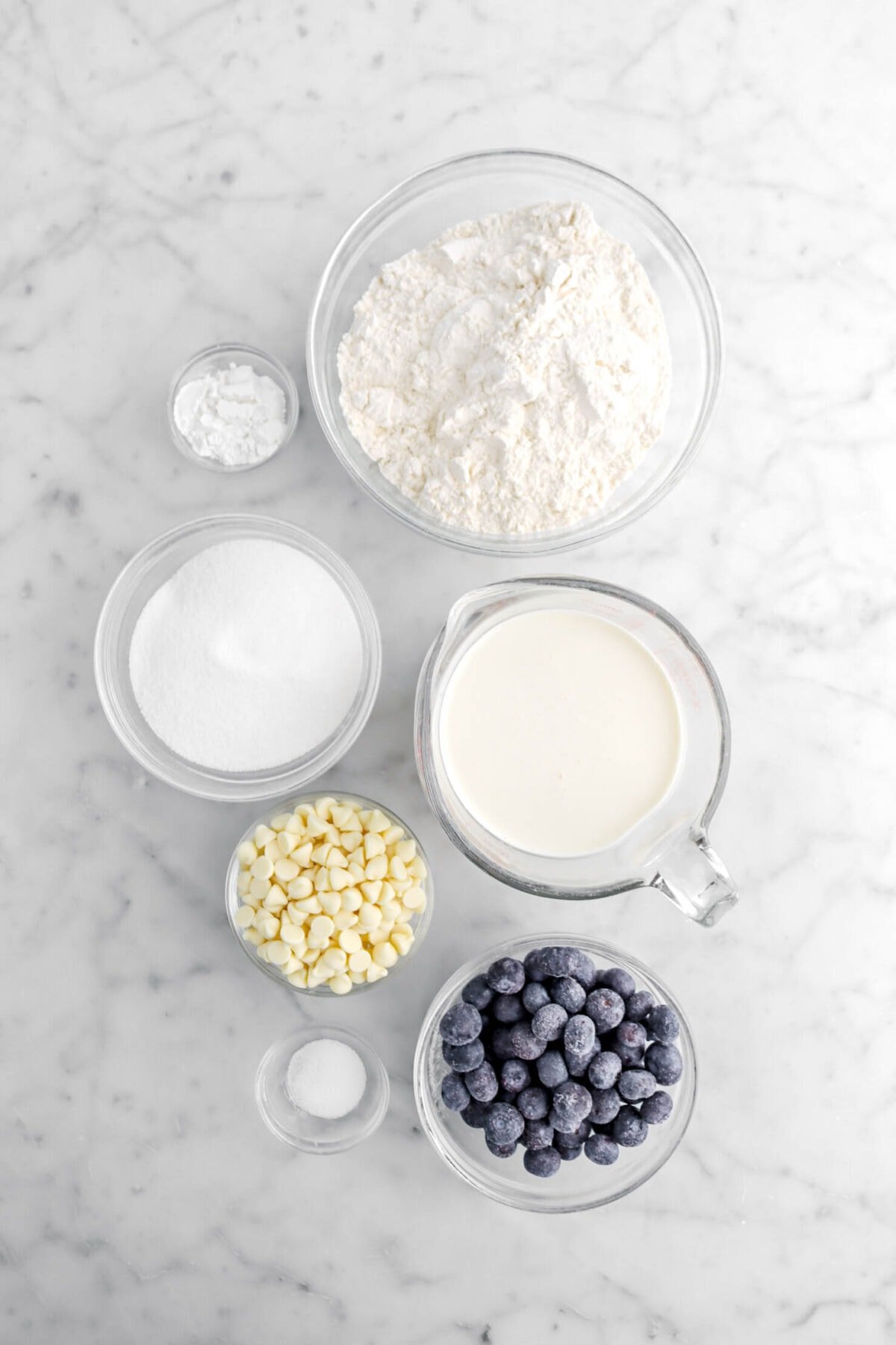 flour, baking poder, sugar, cream, white chocolate, blueberries, and salt on marble surface.