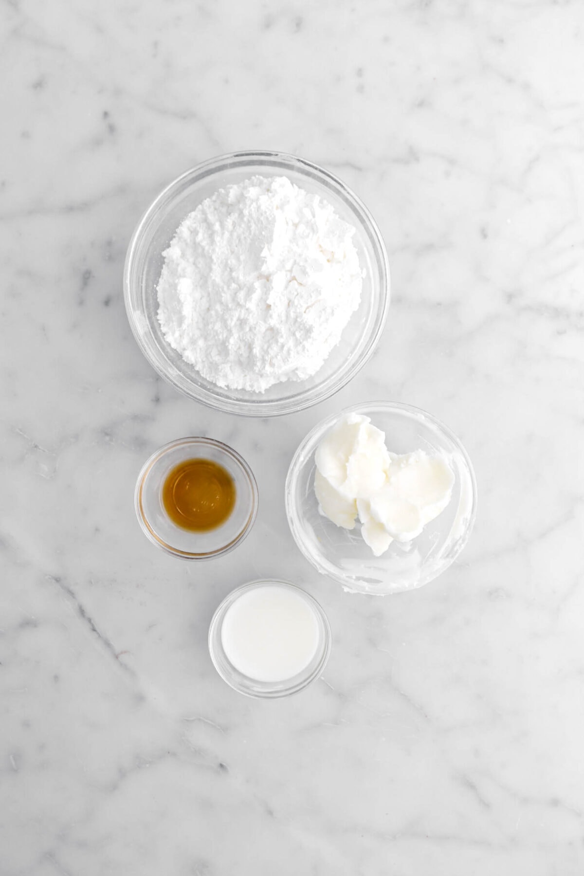 powdered sugar, vanilla, shortening, and milk on marble surface.