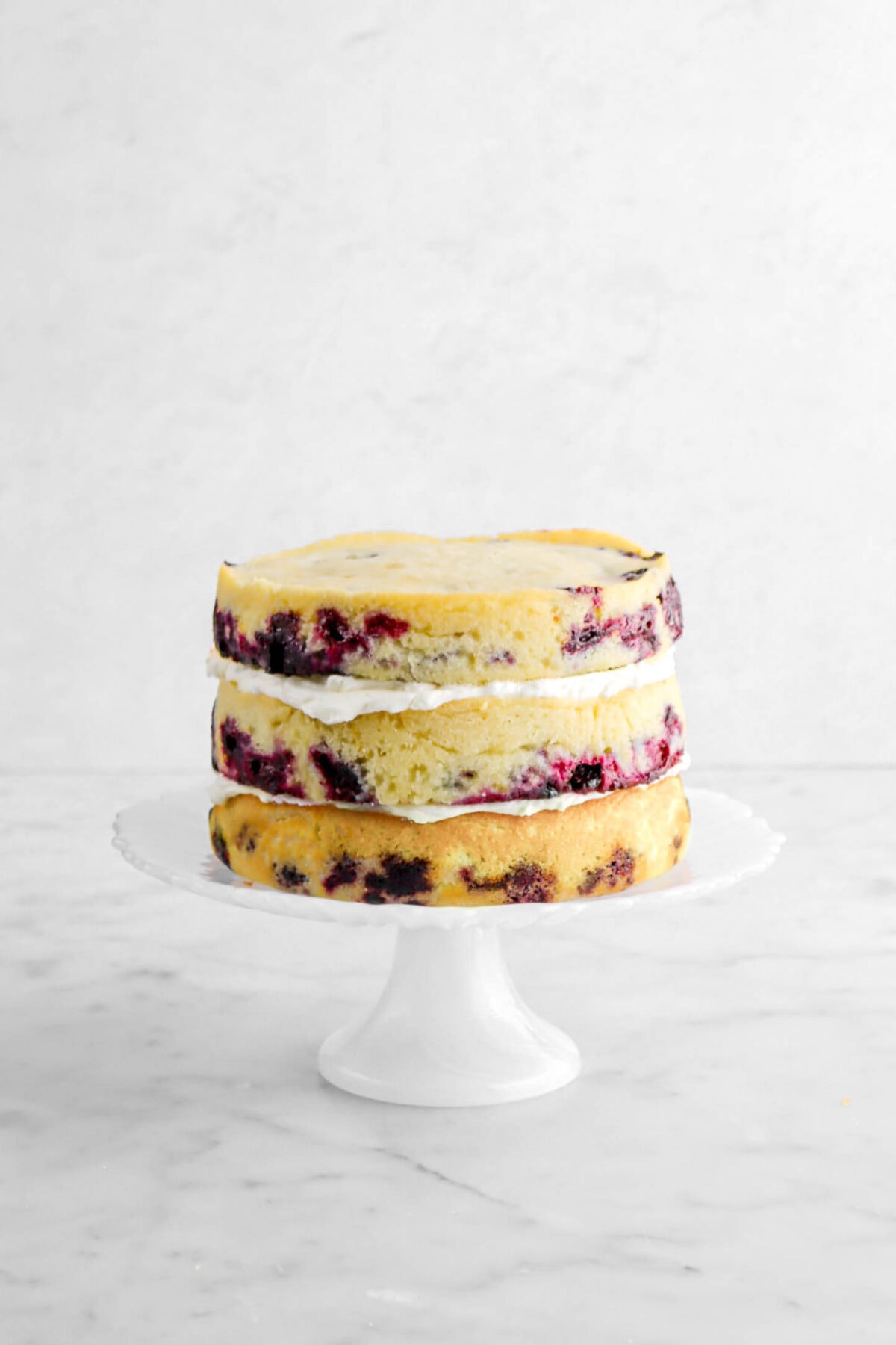three layers of cake with buttercream between each layer on white cake stand.