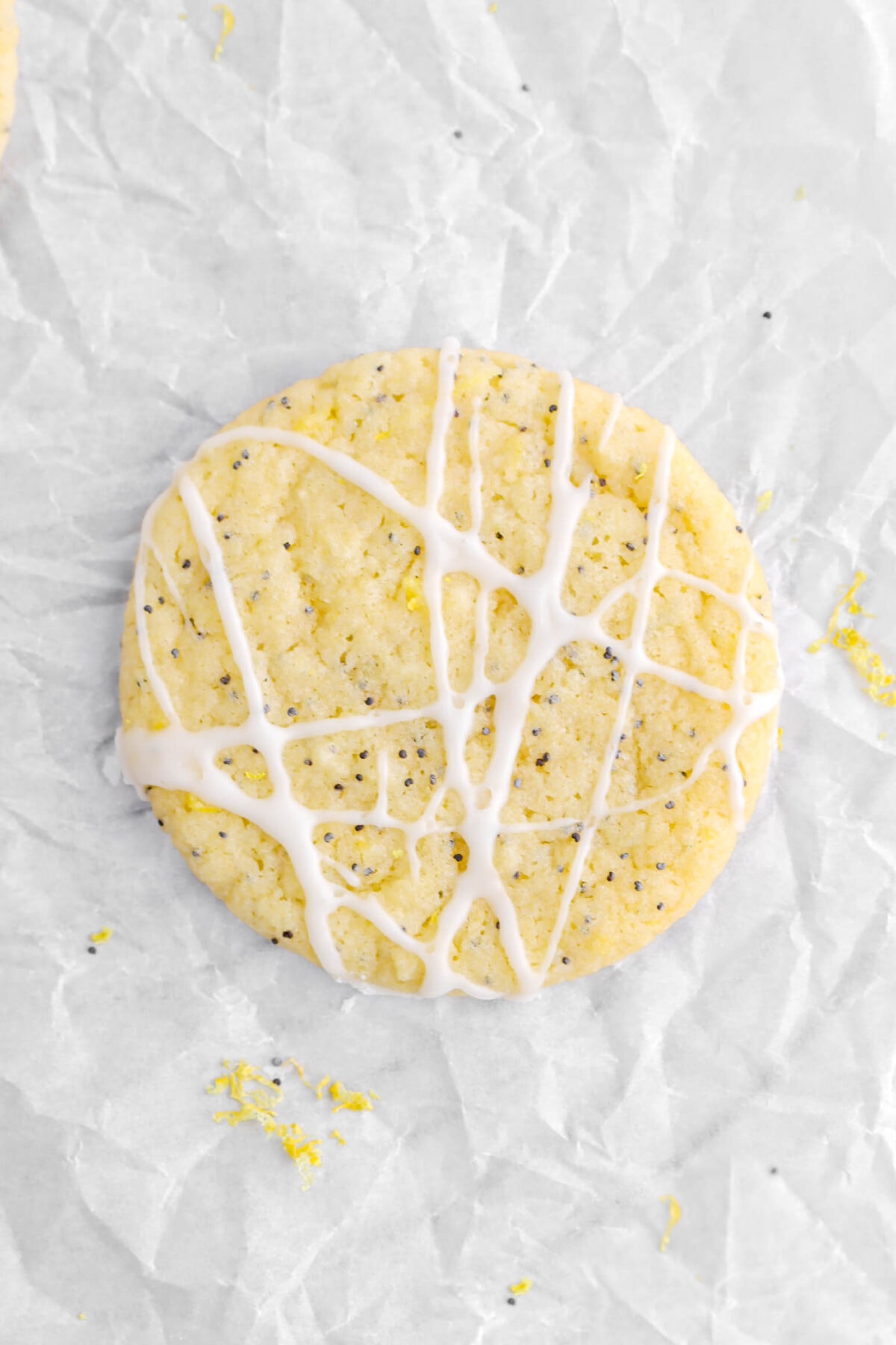 overhead close up of iced lemon poppy seed cookie on parchment paper with lemon zest around.