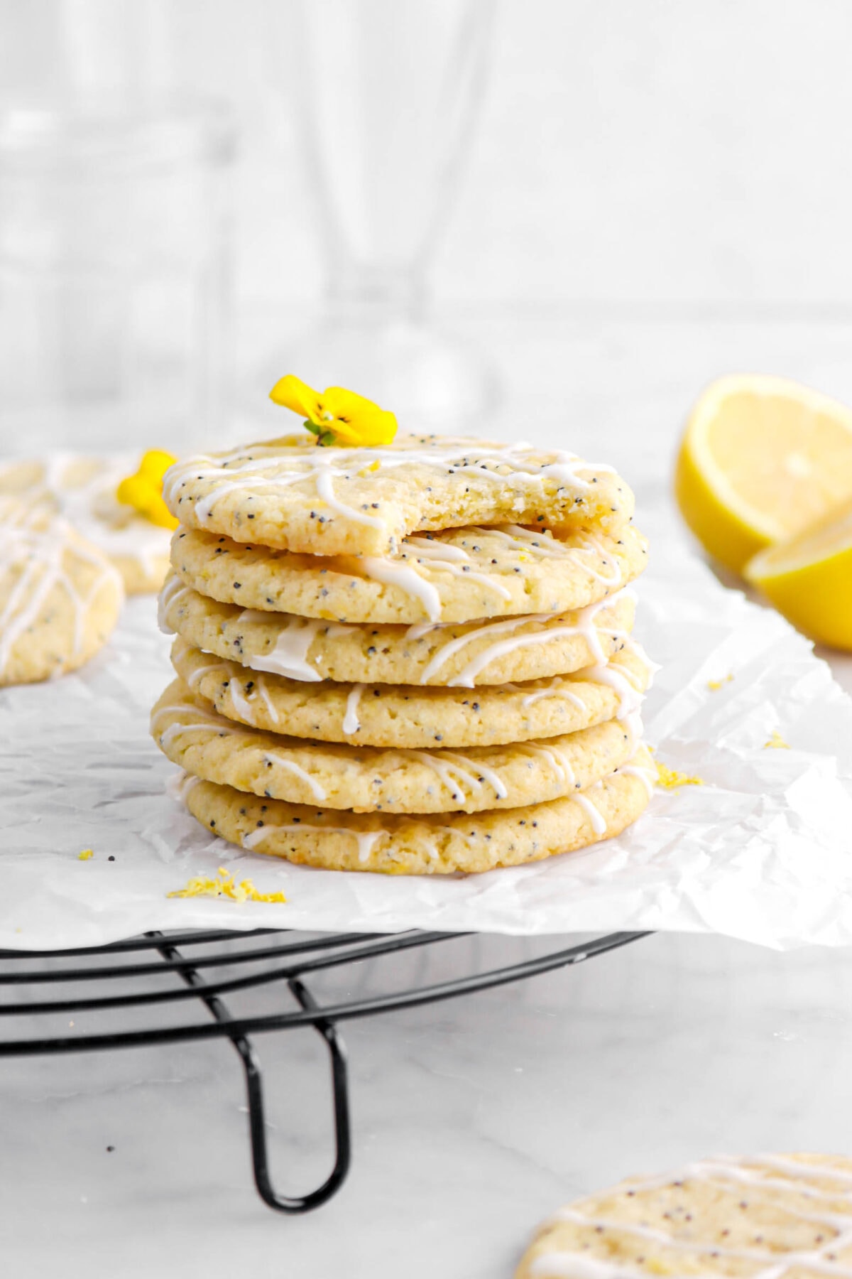 six stacked lemon poppy seed cookies with top cookie missing a bite on a black cooling rack with parchment paper.