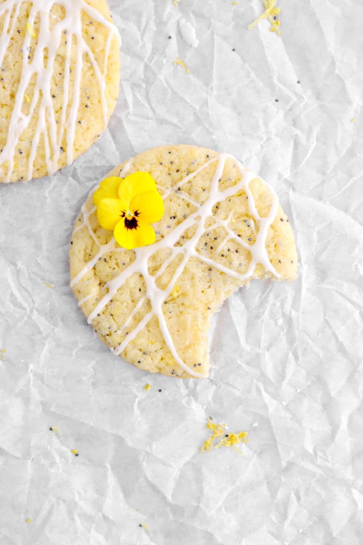 close up overhead shot of lemon poppy seed cookie with bite missing on parchment paper with flower and icing on top.