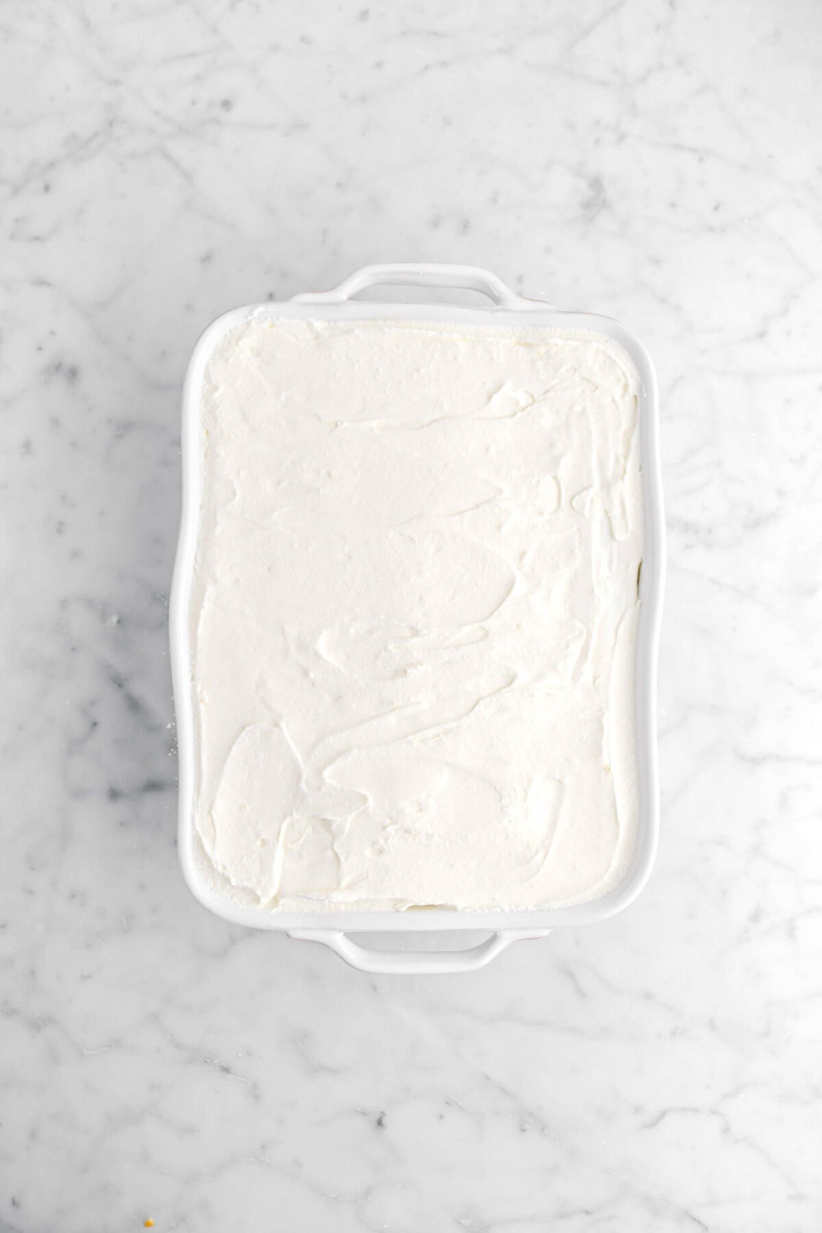 whipped cream spread across ladyfinger layer in white casserole.