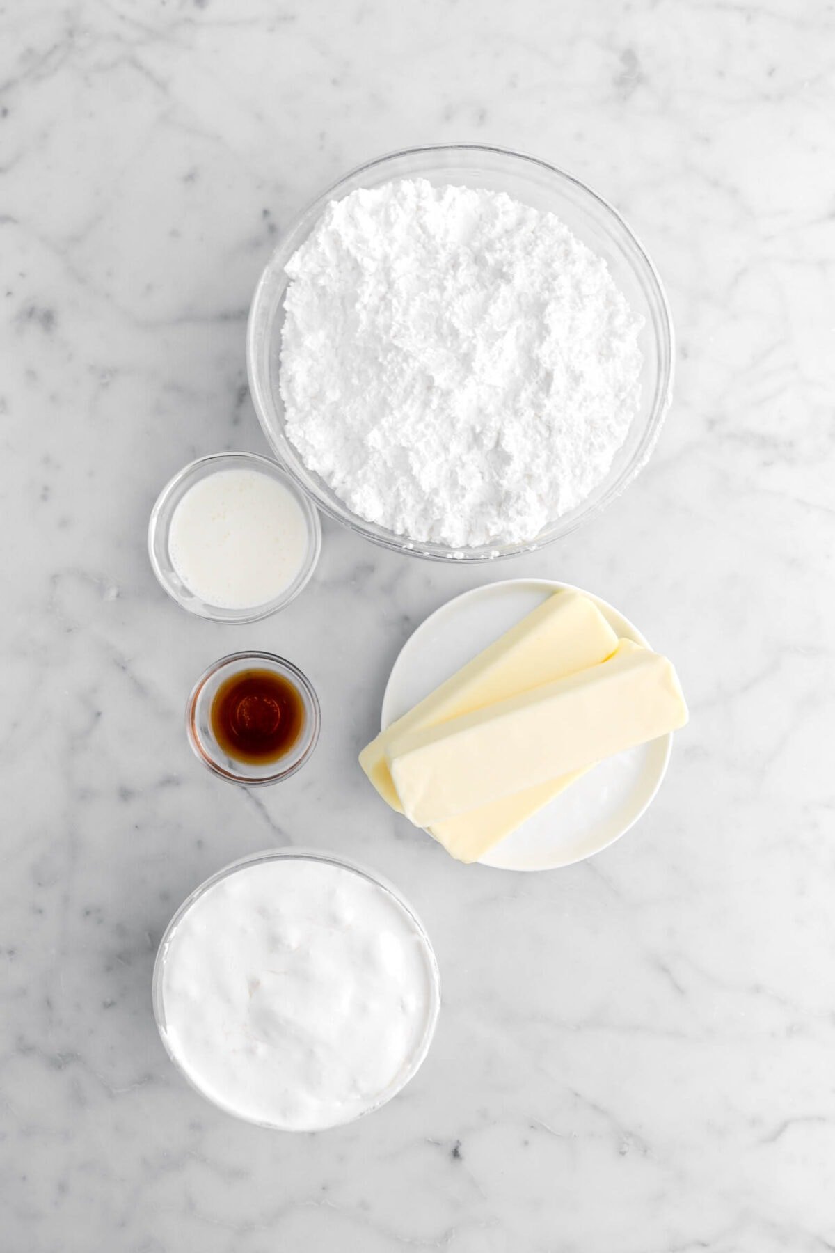 powdered sugar, milk, vanilla, butter, and marshmallow fluff on marble surface.