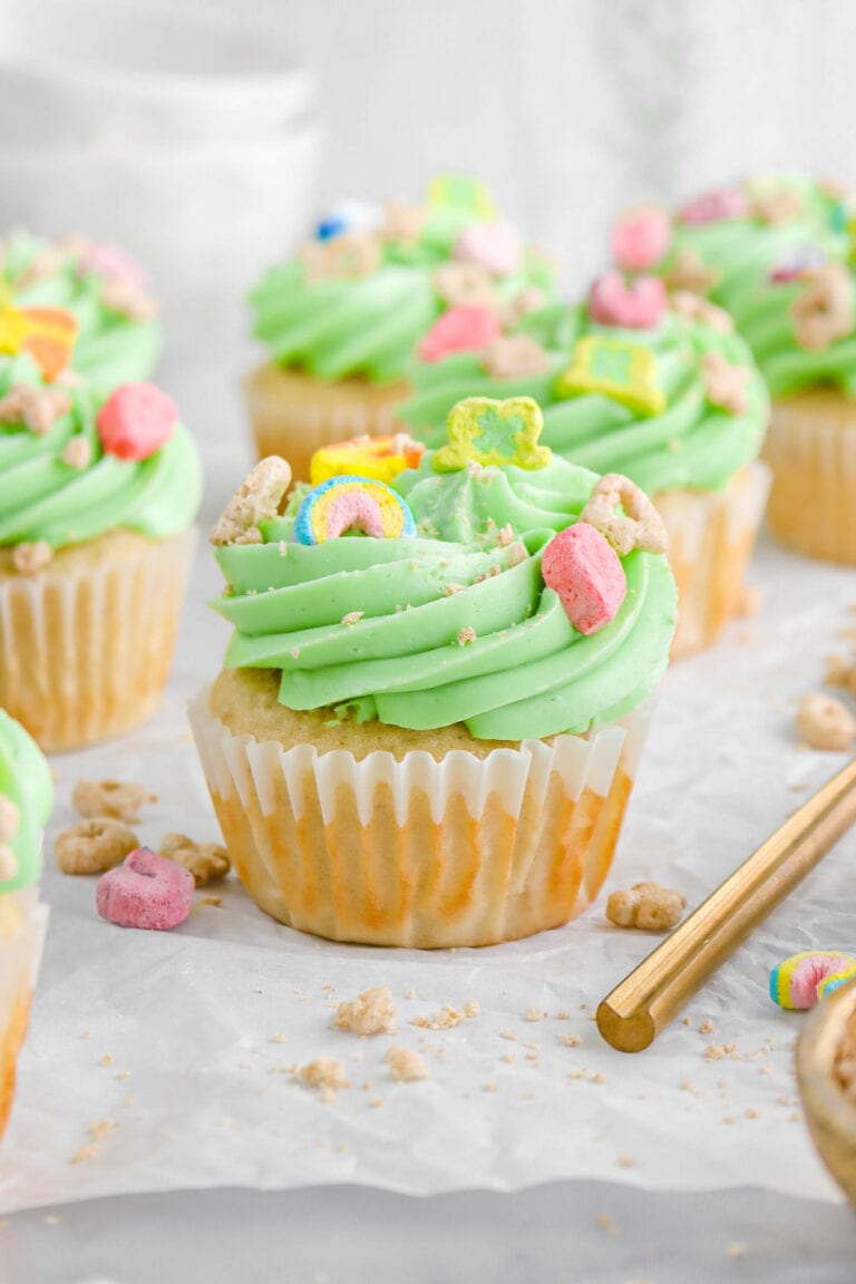 angled close up of lucky charms cupcake on parchment paper with more cupcakes around.