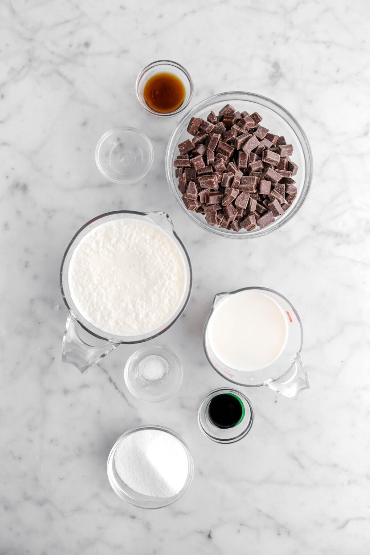 vanilla, peppermint extract, chocolate chunks, milk, cream, salt, green food dye, and sugar on marble surface.