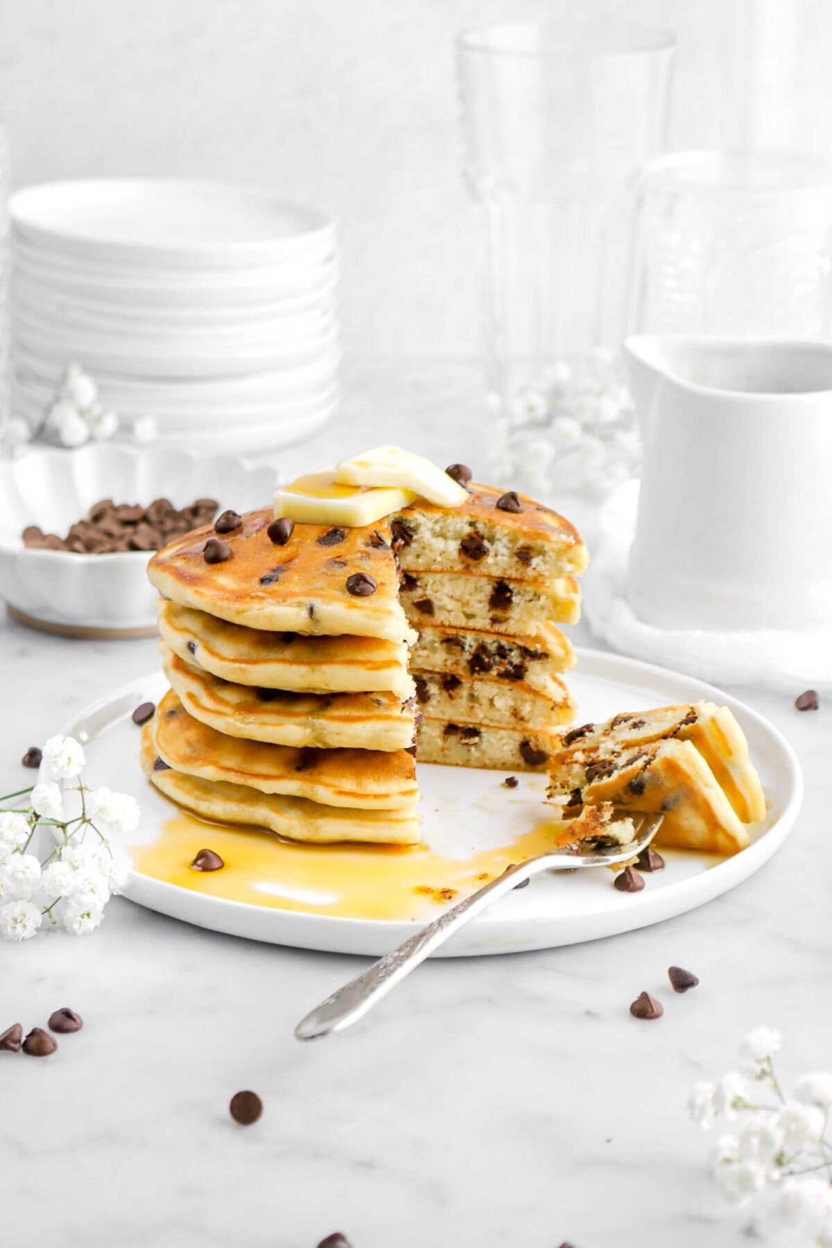 cut chocolate chip pancakes stacked on white plate with forkful of pancake beside.