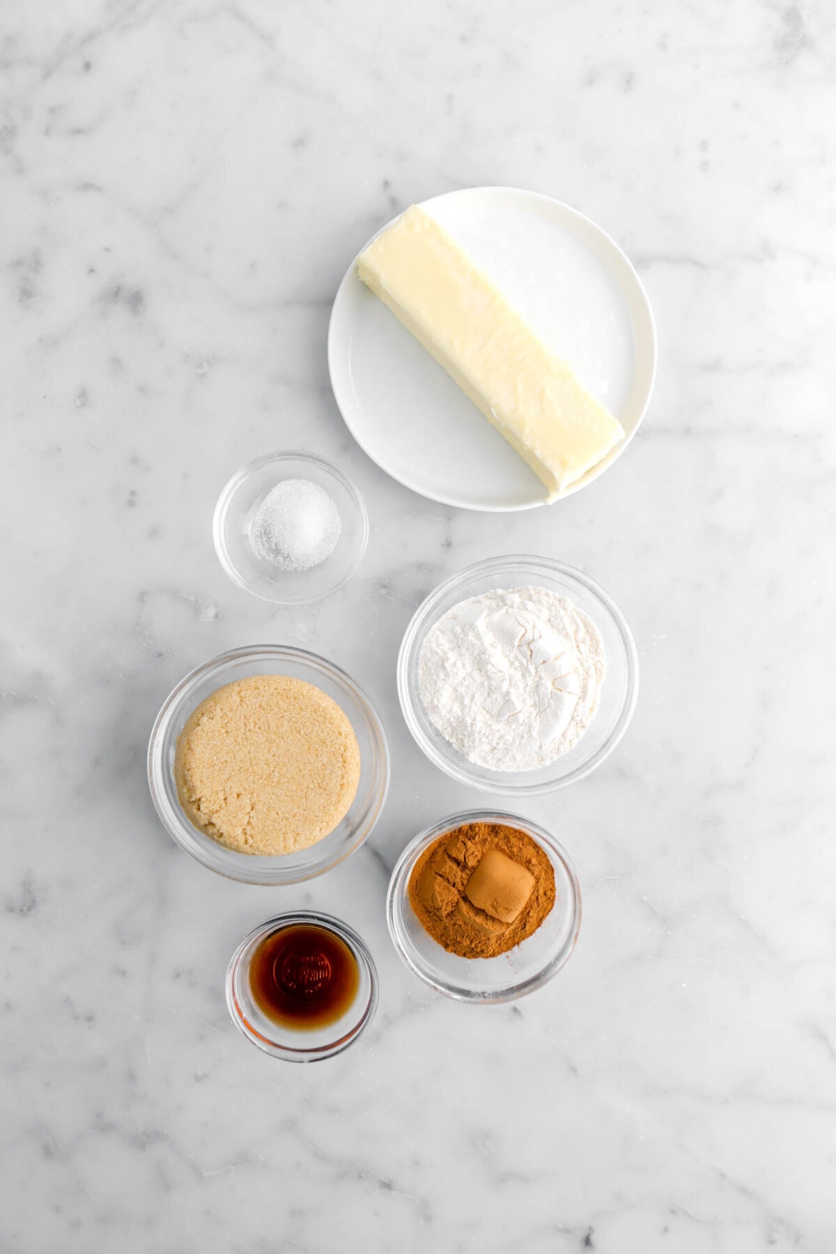 butter, salt, flour, brown sugar, cinnamon, and vanilla on marble surface.