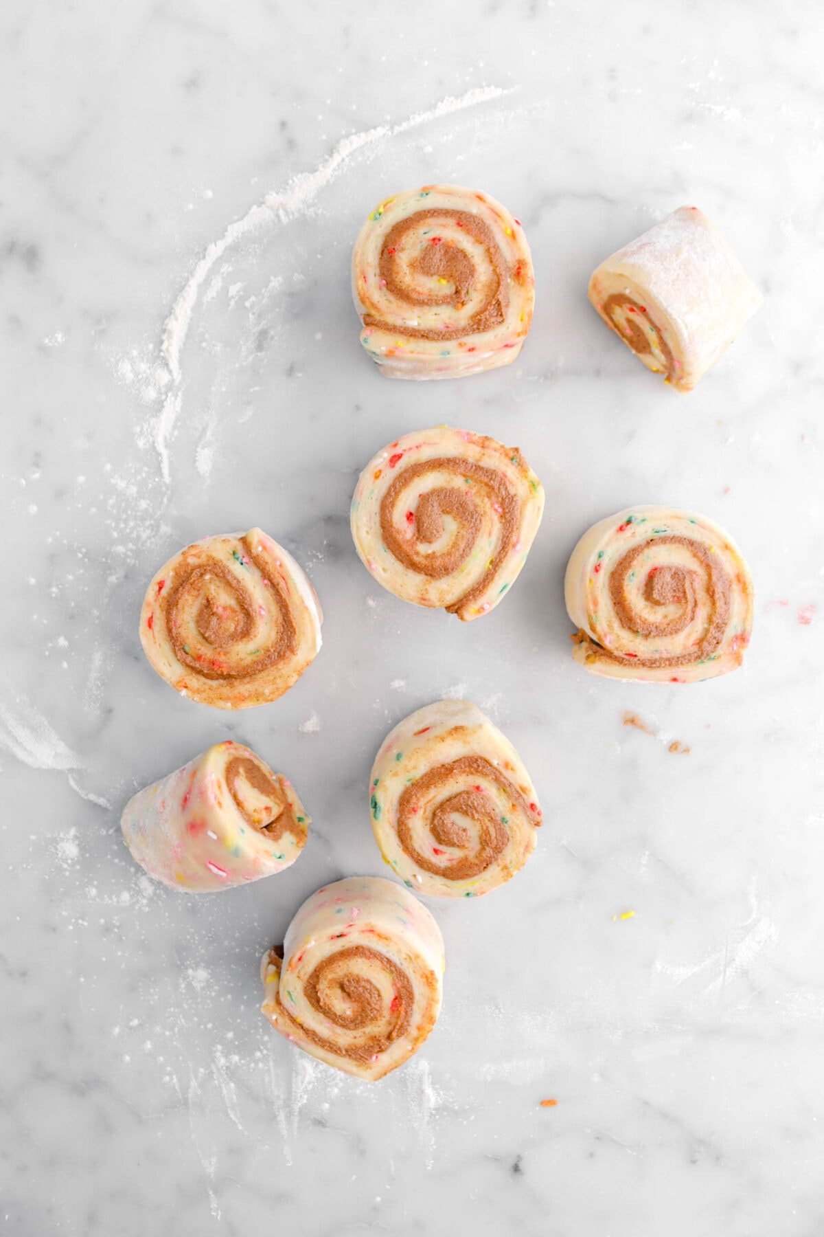 eight unbaked cinnamon rolls on marble surface.