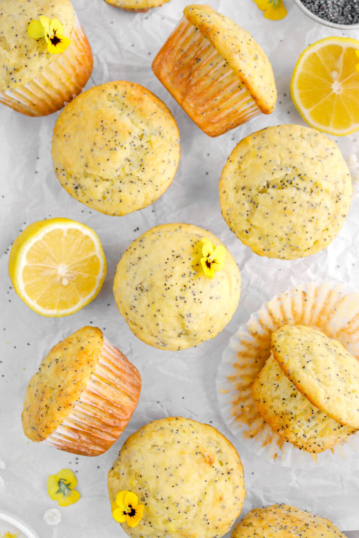lemon poppy seed muffins on parchment paper with lemon halves and yellow pansies.