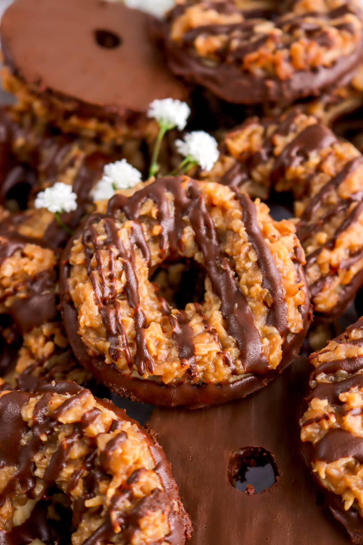 angled close up of samoas cookie with more cookies underneath and white flowers behind.