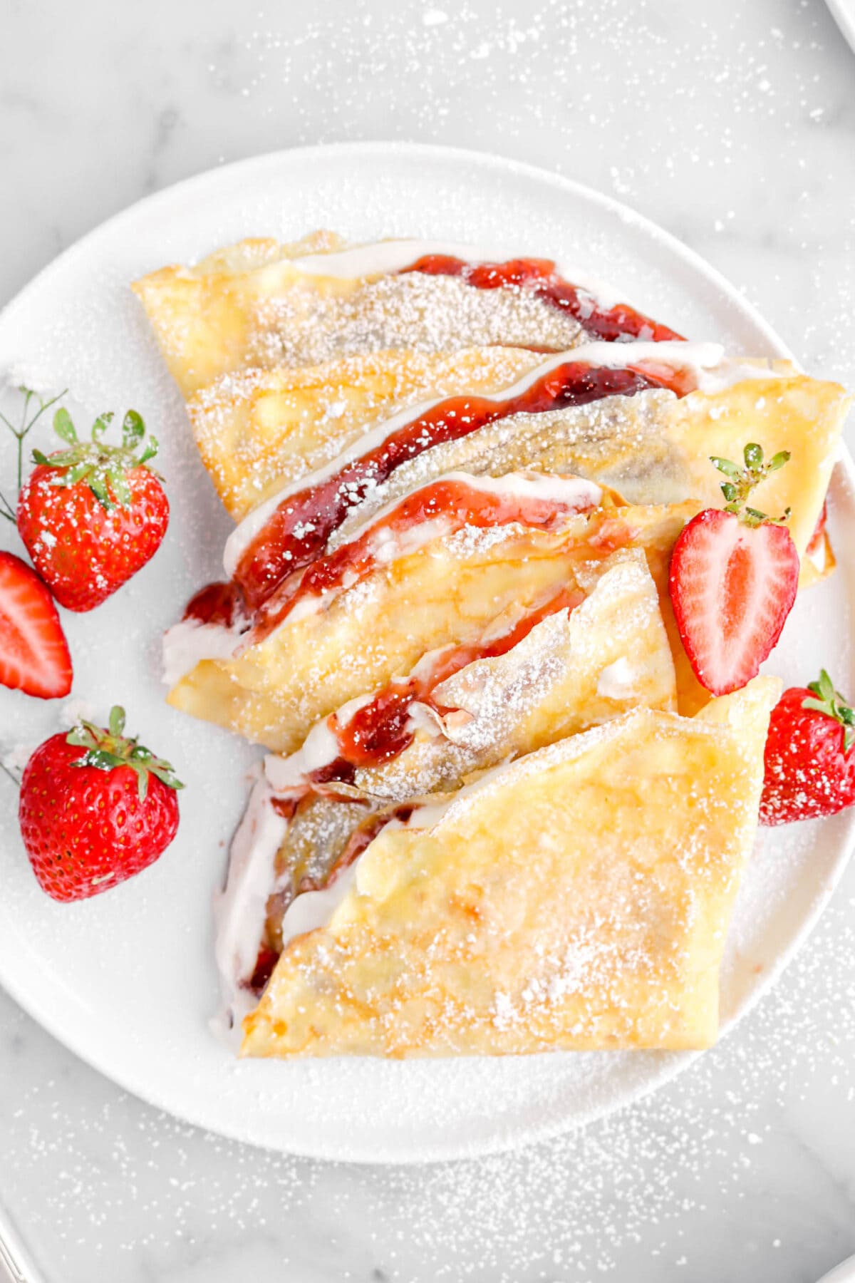 close up of three filled crepes on white plate with strawberries beside.