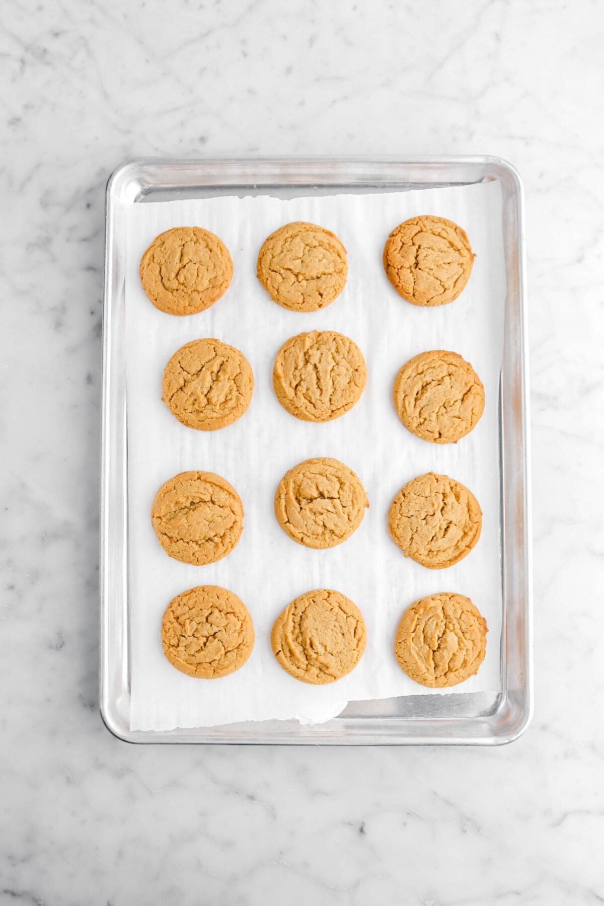 12 baked peanut butter cookies on lined sheet pan.