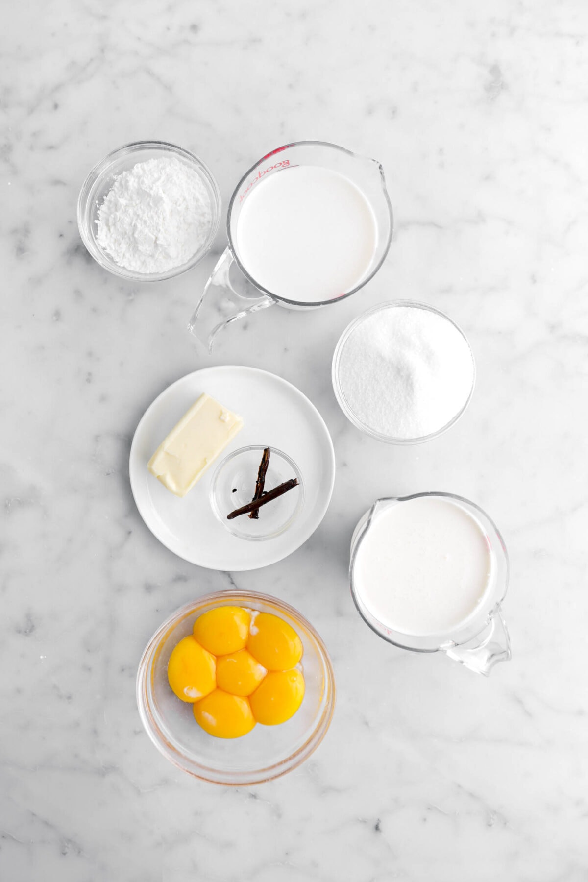 corn starch, milk, sugar, butter, vanilla bean, cream, and egg yolks on marble surface.