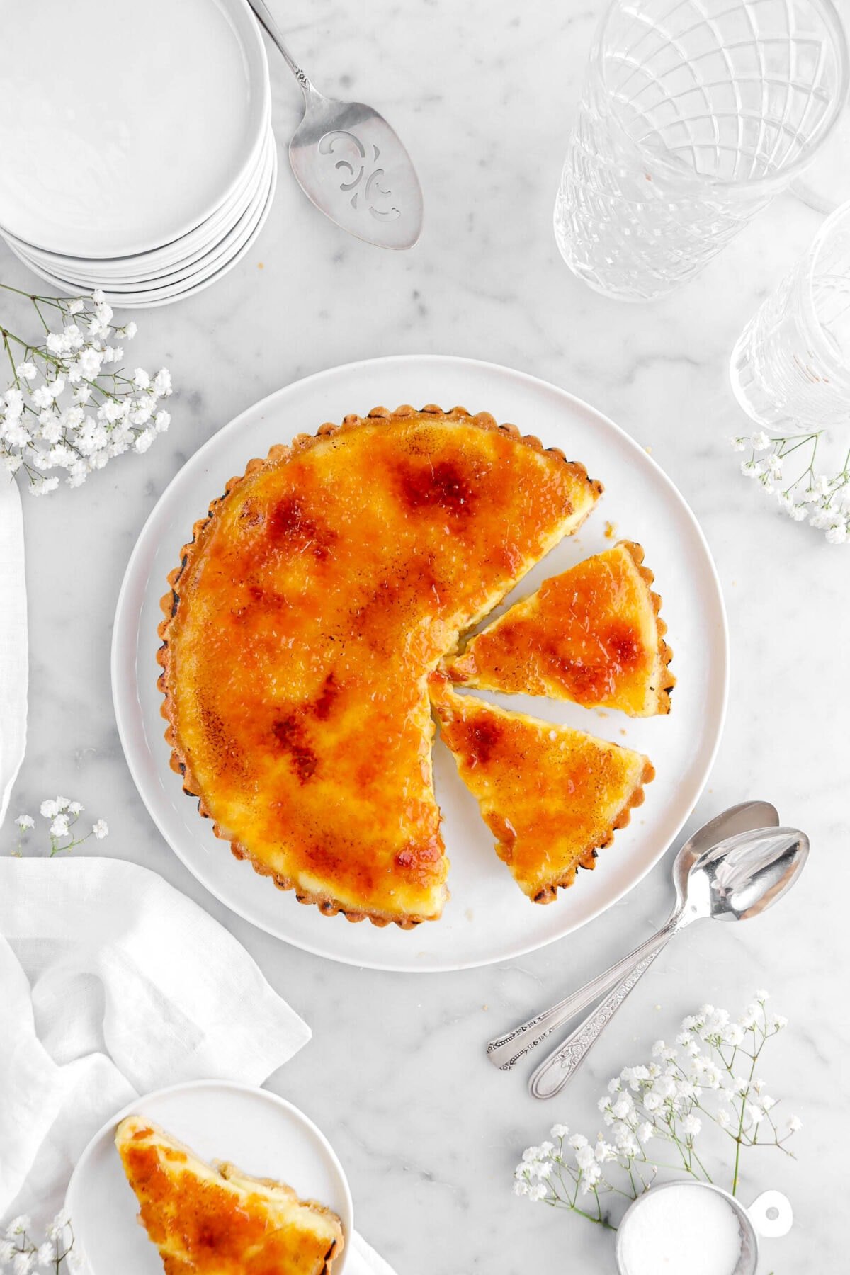 overhead shot of tart with two slices cut into it on white plate with another slice beside on smaller white plate with flowers around.