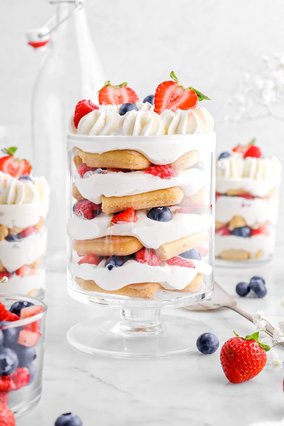 close up of berry trifle with piped whipped cream and berries on top, more berries around, and two trifles behind.