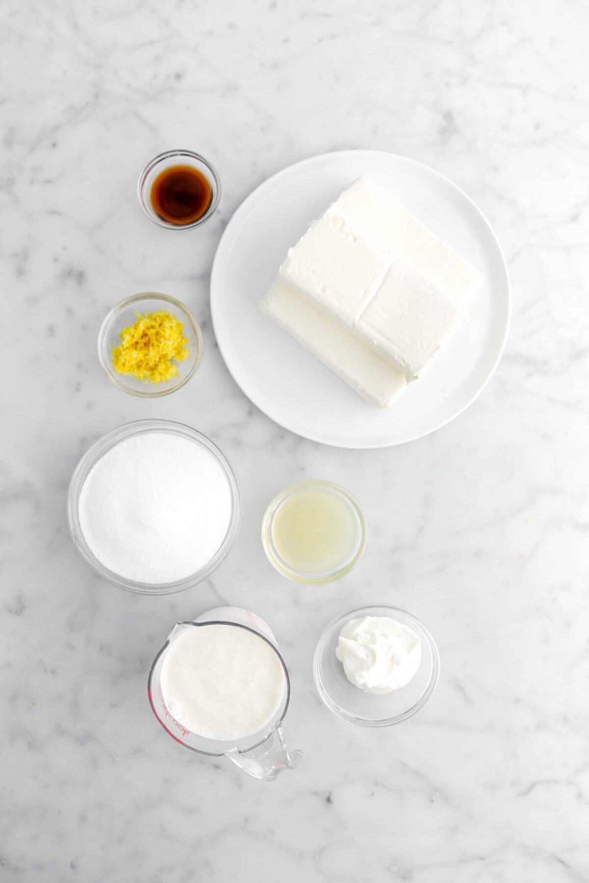 vanilla, cream cheese, lemon zest, sugar, lemon juice, cream, and sour cream on marble surface.