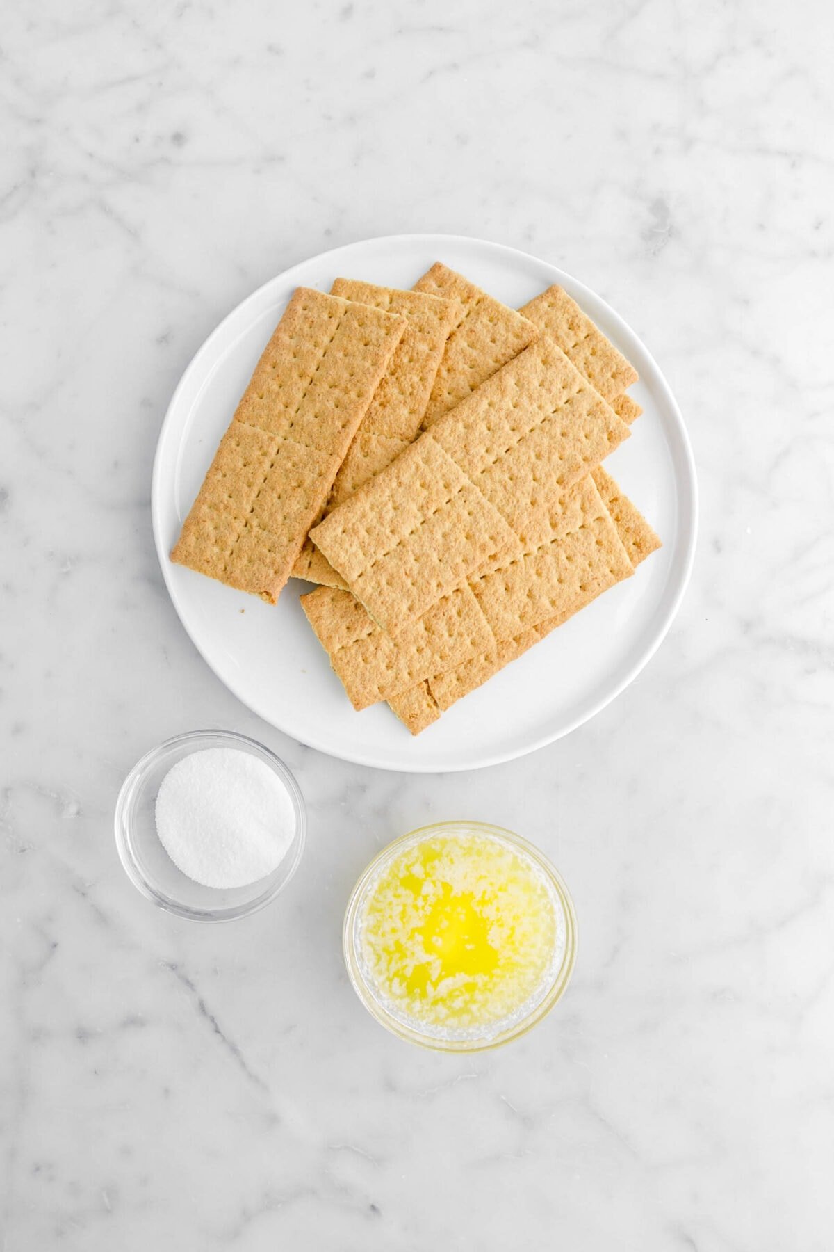 graham crackers, sugar, and melted butter on marble surface.