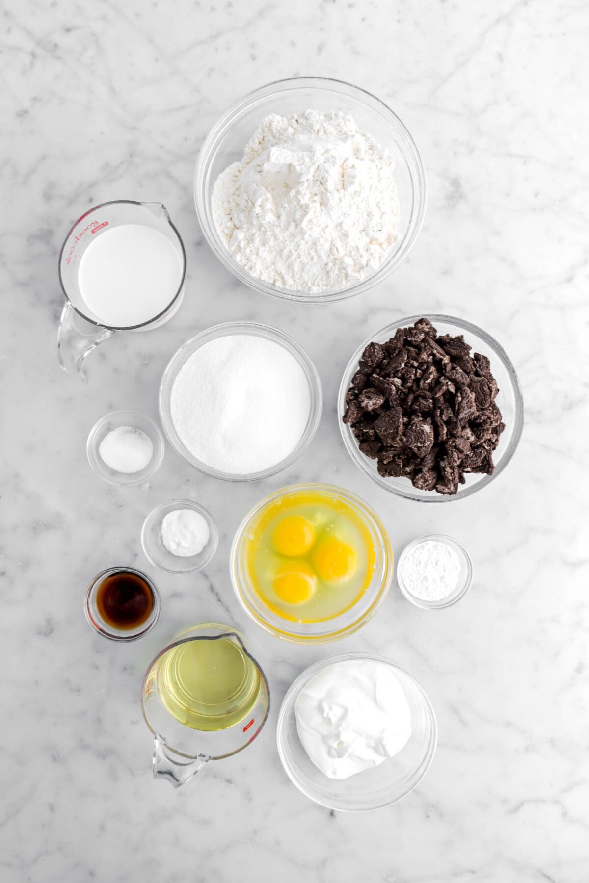milk, flour, oreo chunks, sugar, salt, baking soda, eggs, baking powder, vanilla, vegetable oil, and sour cream on marble surface.