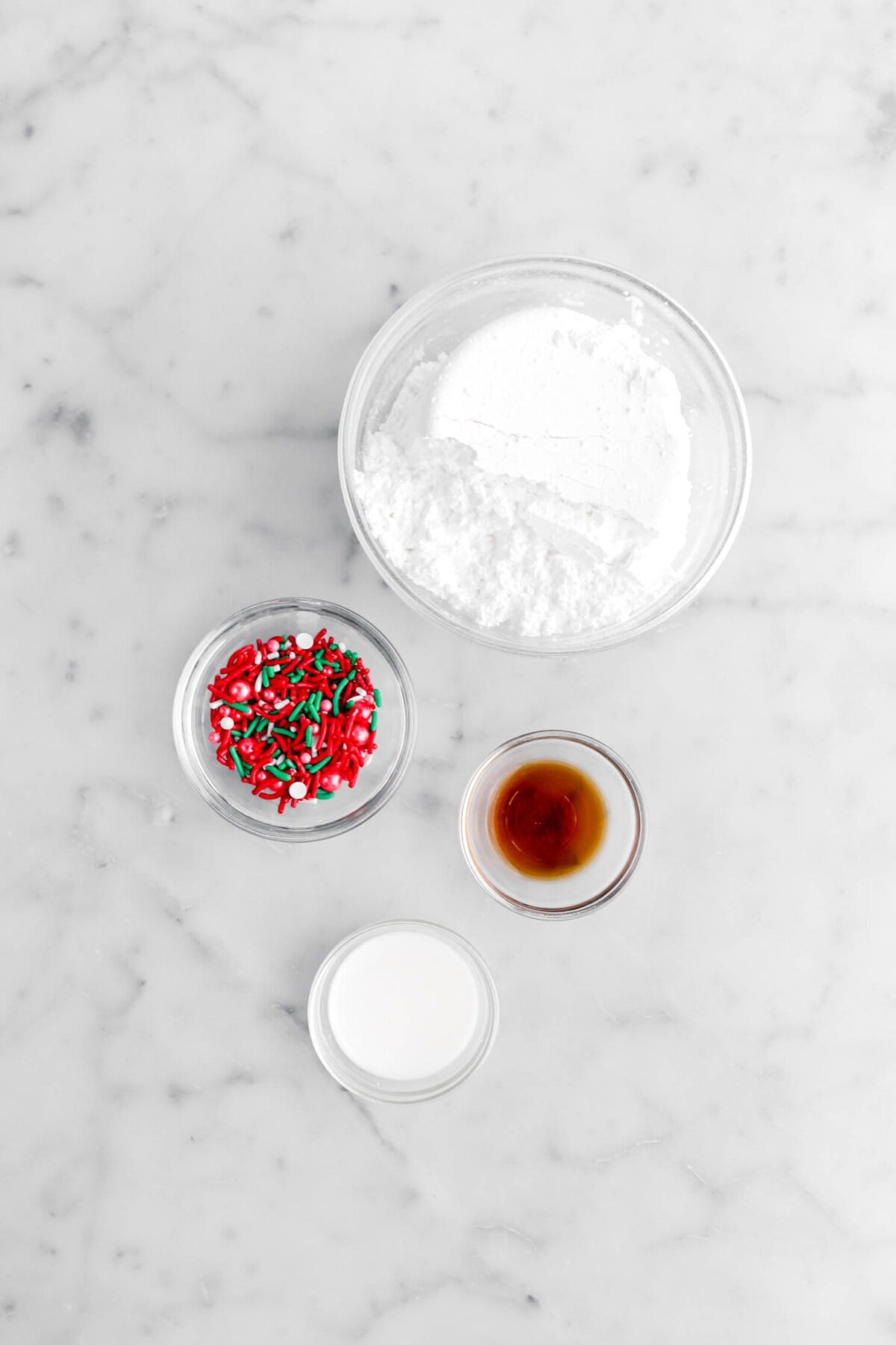 powdered sugar, red, green, and white sprinkles, vanilla, and milk on marble surface.