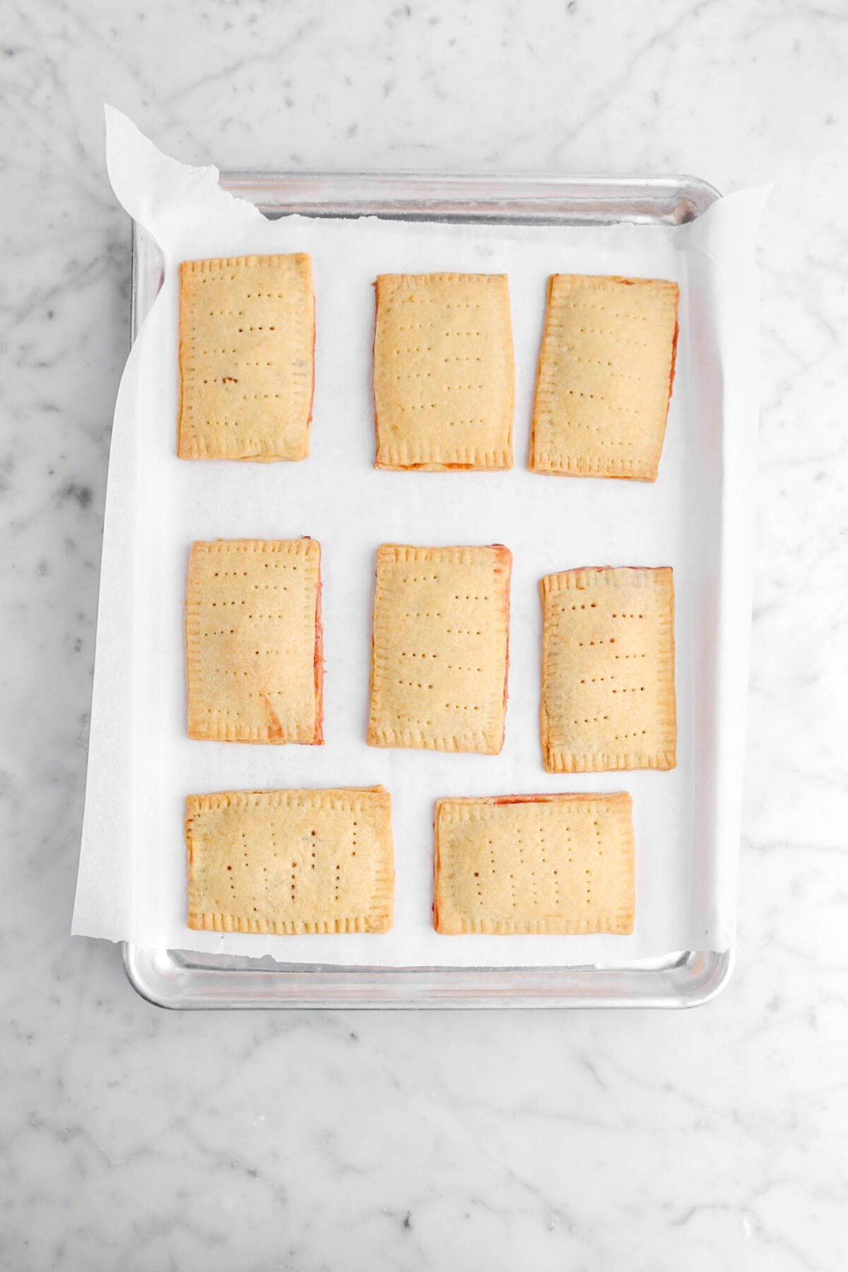 eight baked and un-iced pop tarts on lined sheet pan.