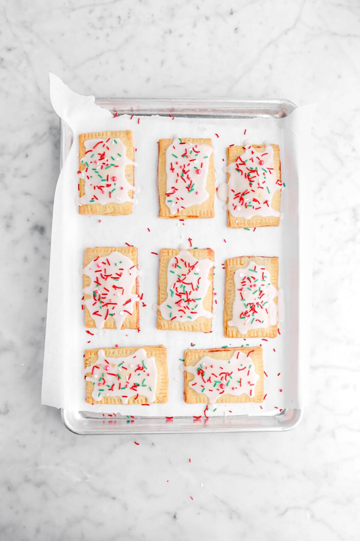 iced pop tarts with sprinkles on top on lined sheet pan.