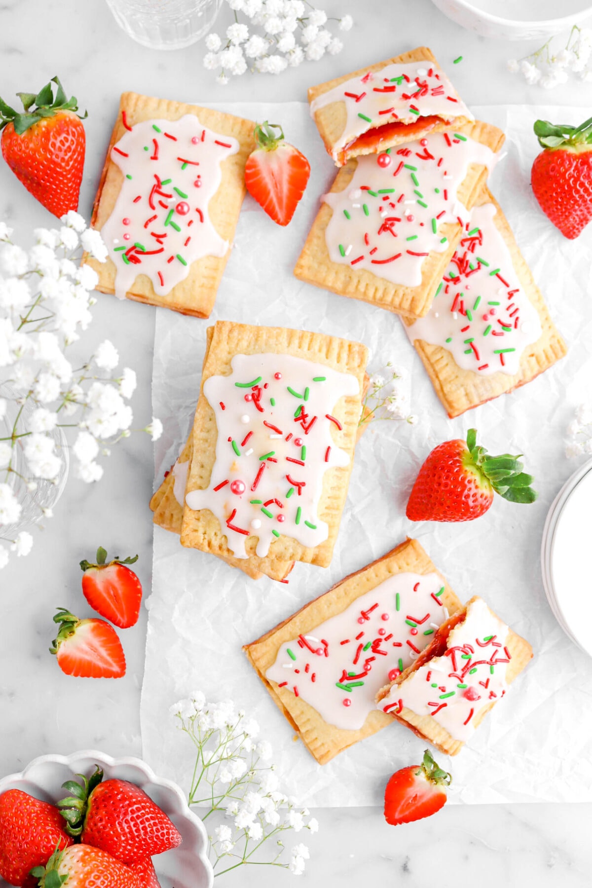 eight iced strawberry pop tarts on parchment paper with one pop tart broken in half and propped against other pop tarts to expose the jam filling.