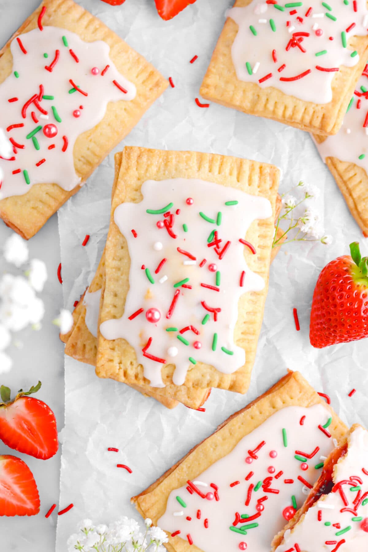 close up overhead shot of three stacked pop tarts with more around, white flowers, and a strawberry.