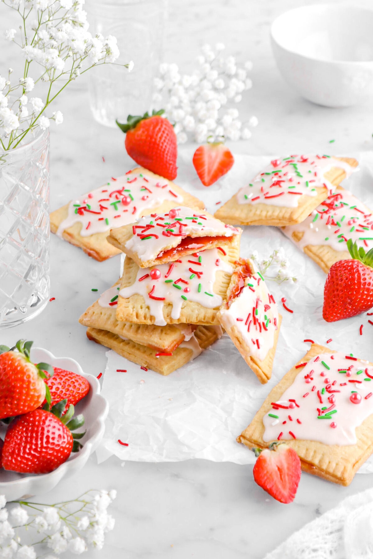 angled shot of stacked pop tarts with top pop tart broken in half with more pop tarts around, white flowers, and fresh strawberries.