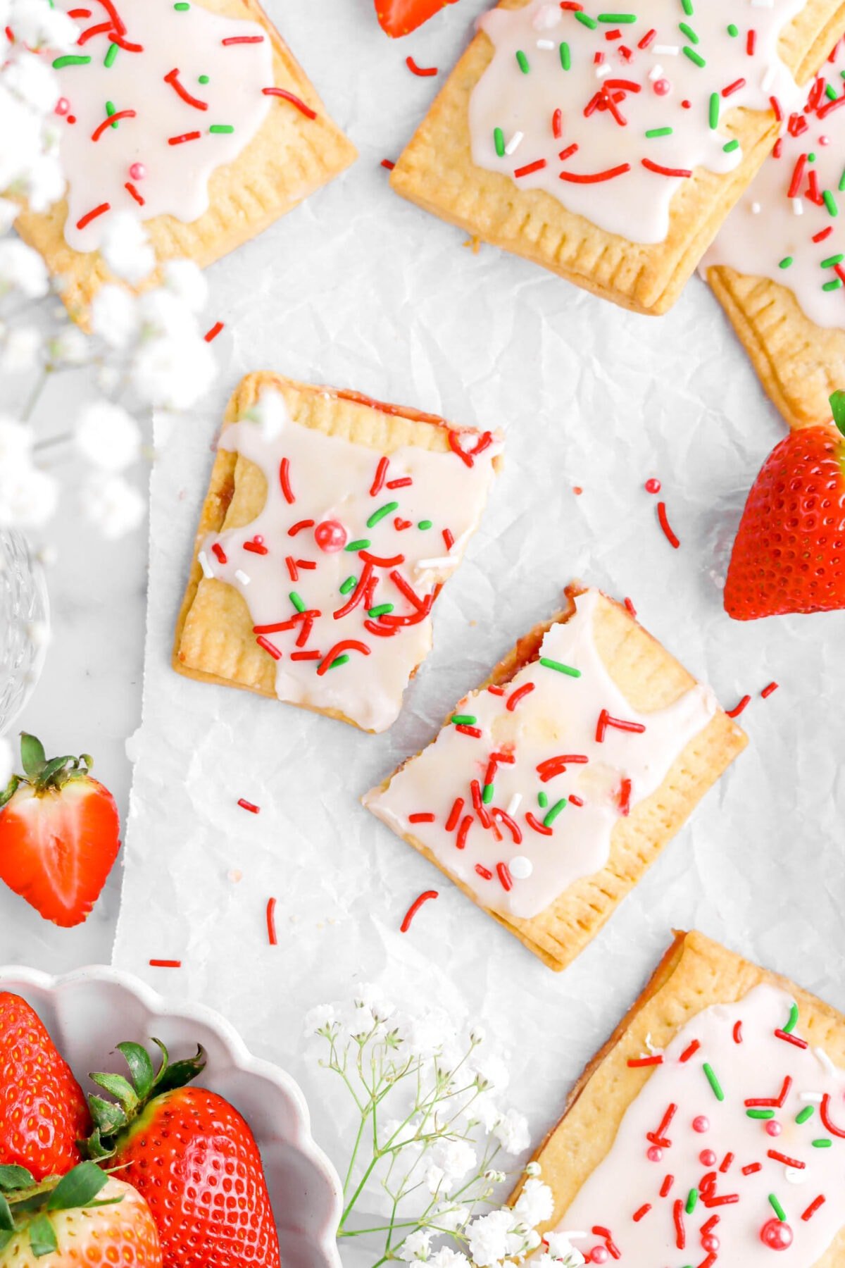 two halves of strawberry pop tart on parchment paper with more pop tarts and strawberries around.
