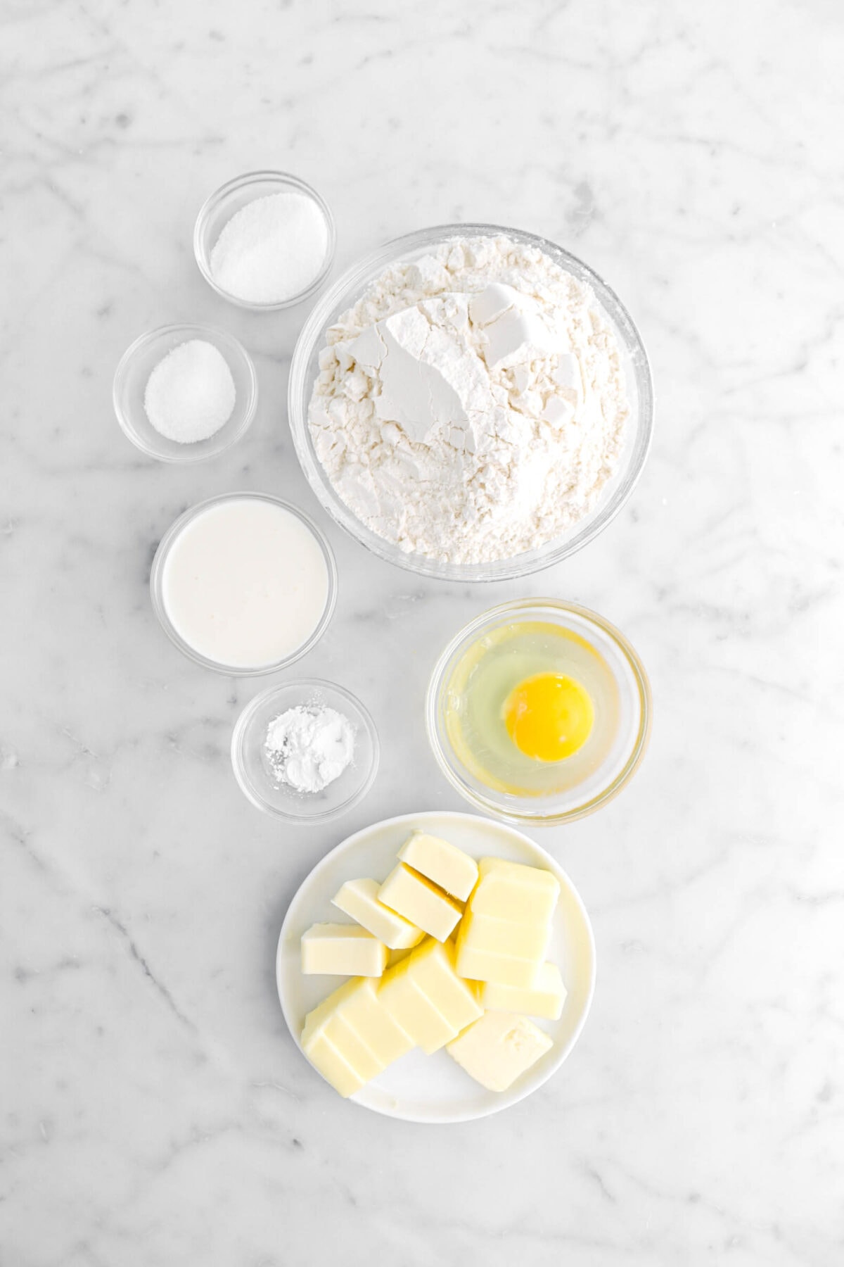sugar, salt, milk, flour, baking powder, egg, and butter on marble surface.